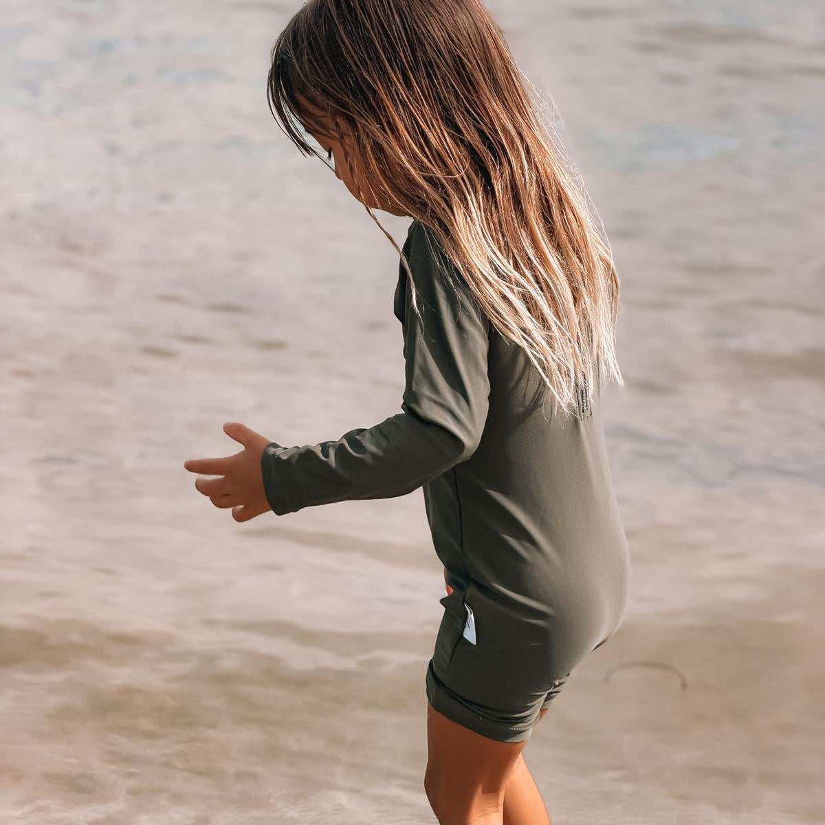 Child playing in shallow water wearing a green swimsuit.