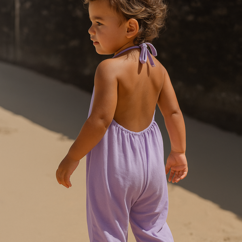 Child wearing a light purple romper standing on sand with a dark background