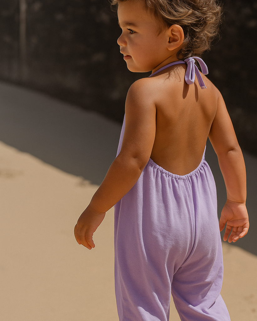 Child wearing a light purple romper standing on sand with a dark background