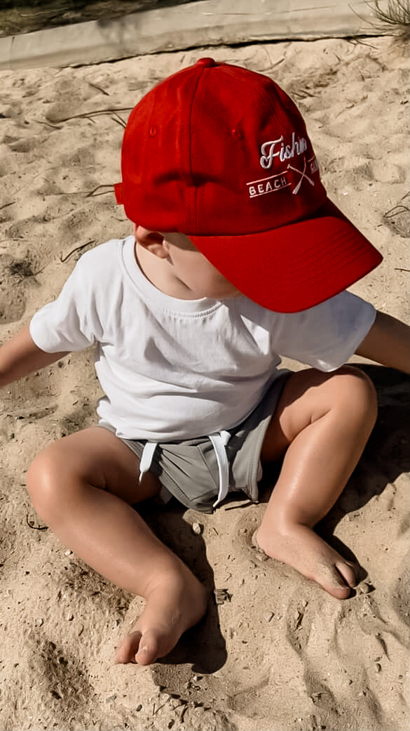 Child wearing a red cap with branding sitting on sand