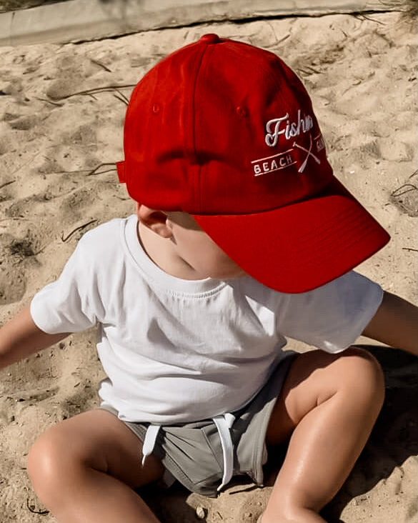Child wearing a red cap with branding sitting on sand
