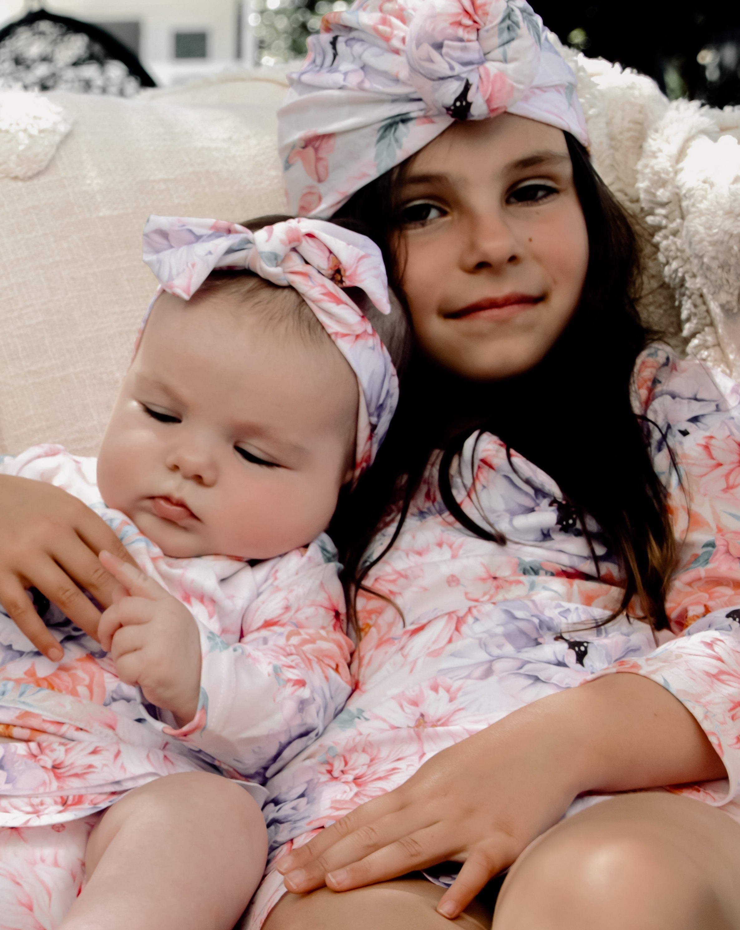 A baby and young girl in long sleeve floral swimwear that is matching