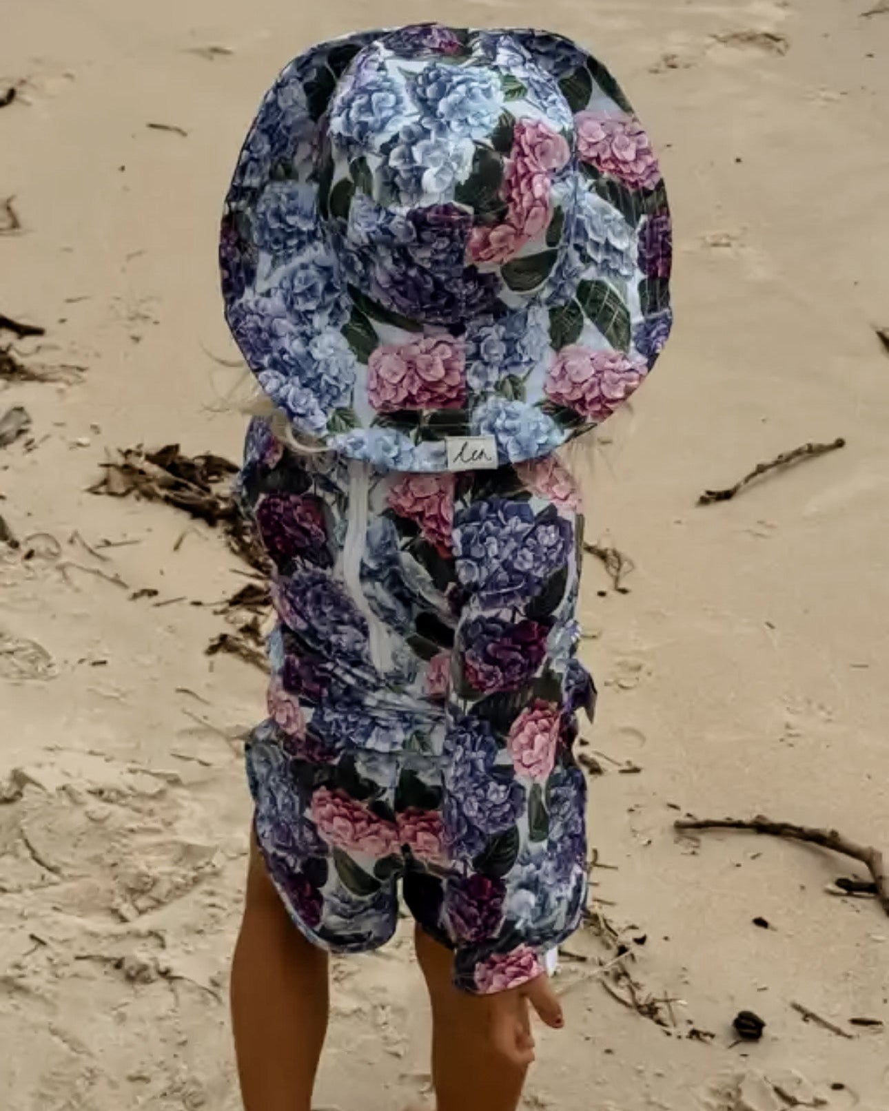 Child wearing a floral swim sun hat and rash swim set on a sandy beach.
