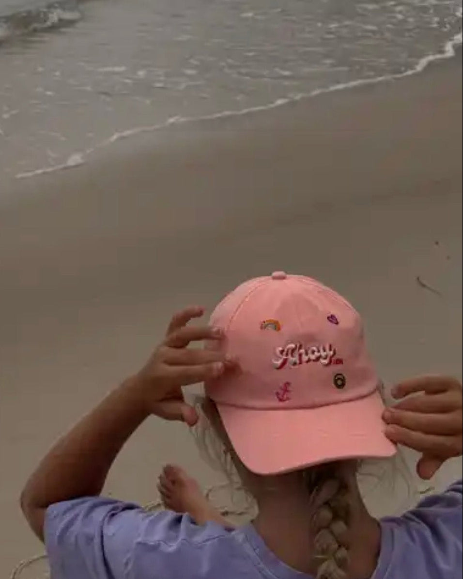 Person holding a pink cap with 'ahoy' text on a beach