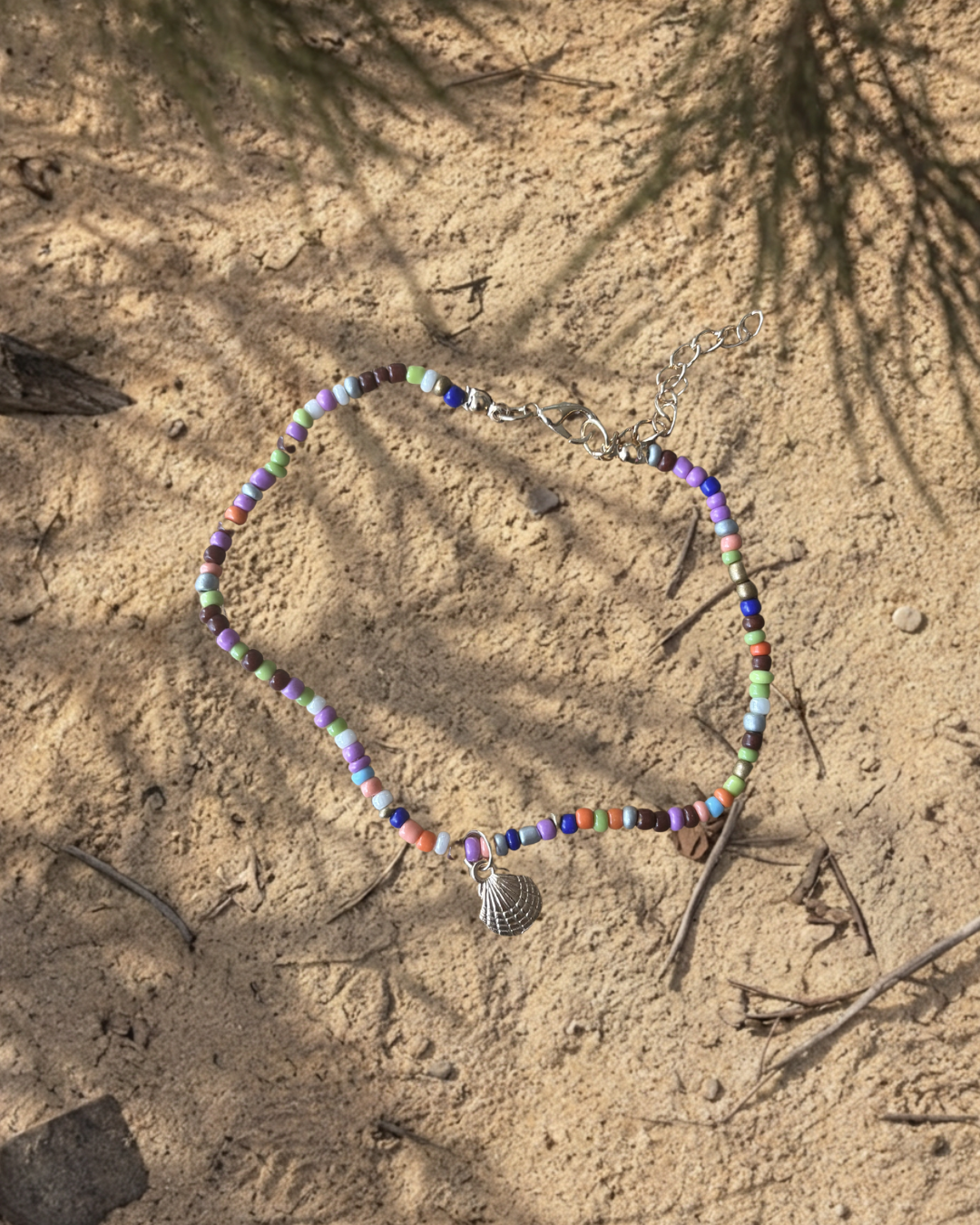 Colorful beaded necklace with a shell pendant on sandy ground