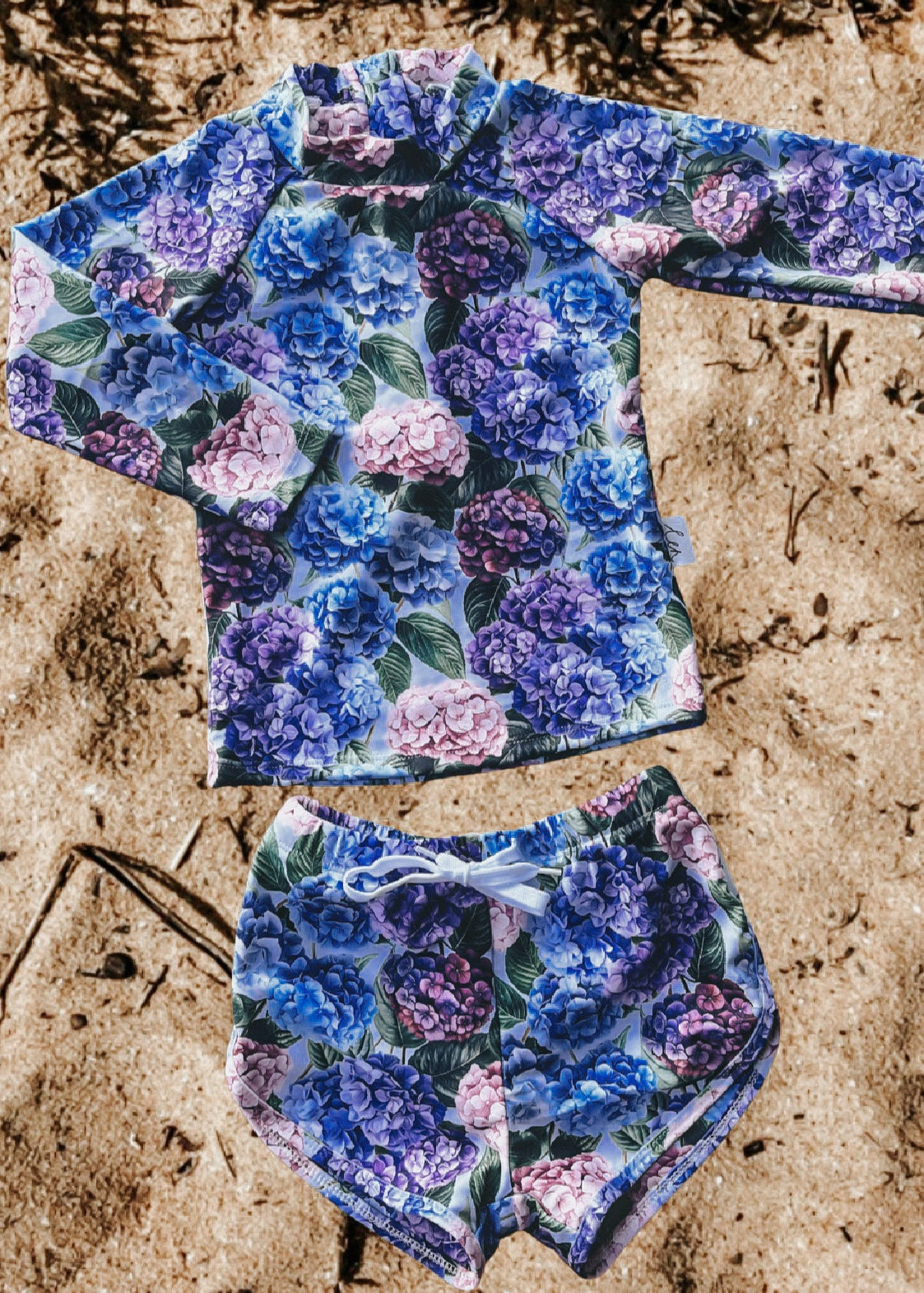 Floral patterned long-sleeve girls rash swim top and shorts set on sandy surface