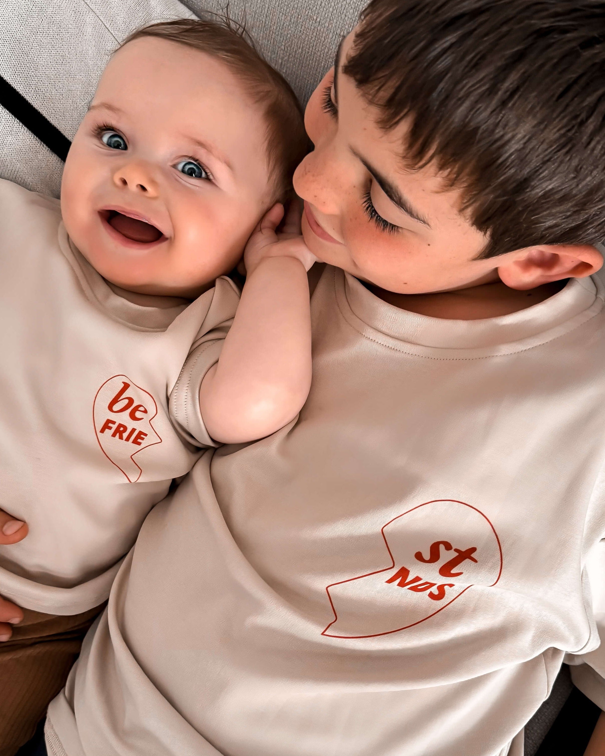 Two children wearing matching t-shirts with visible text, sitting close together.