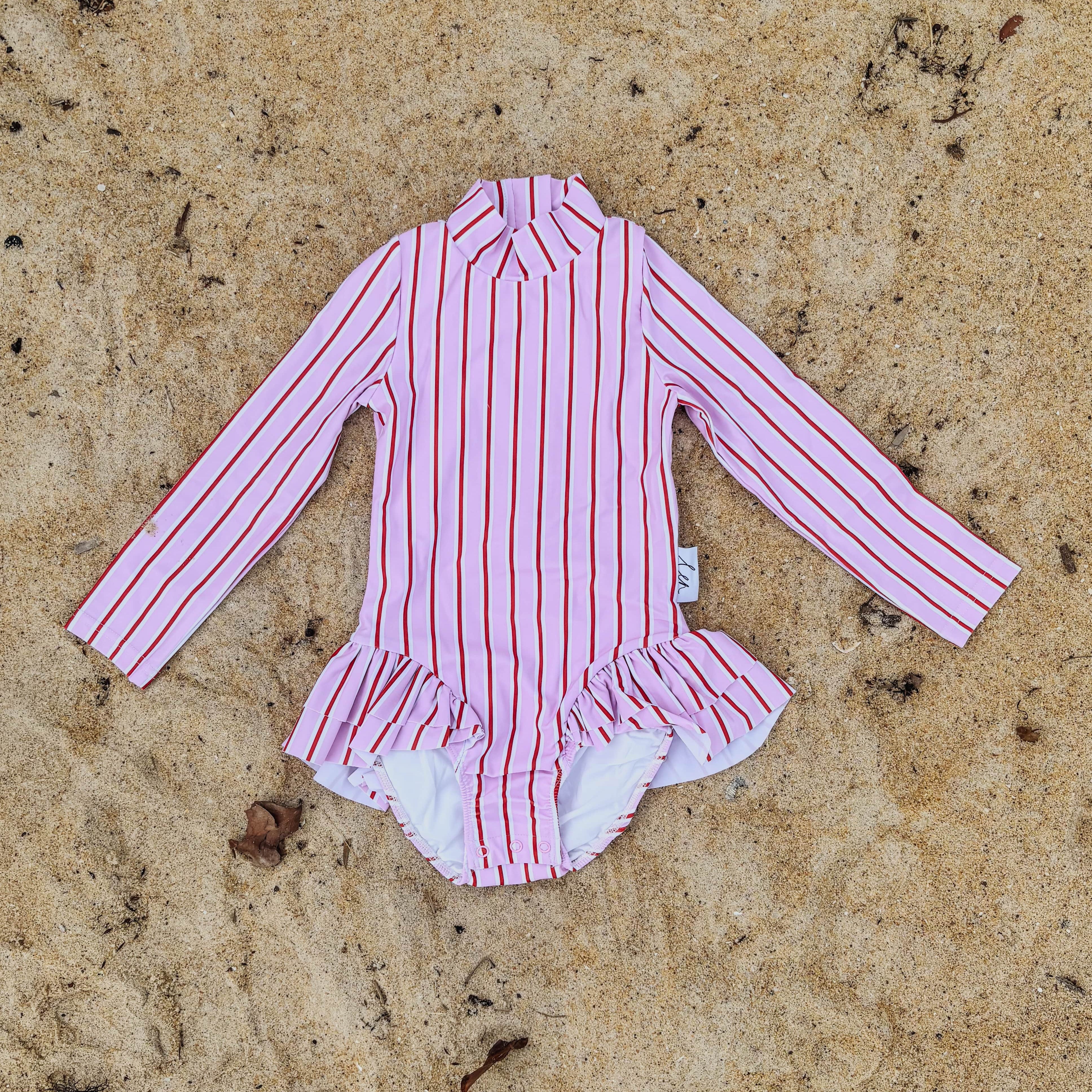Pink, red and white striped swimsuit on a sandy surface
