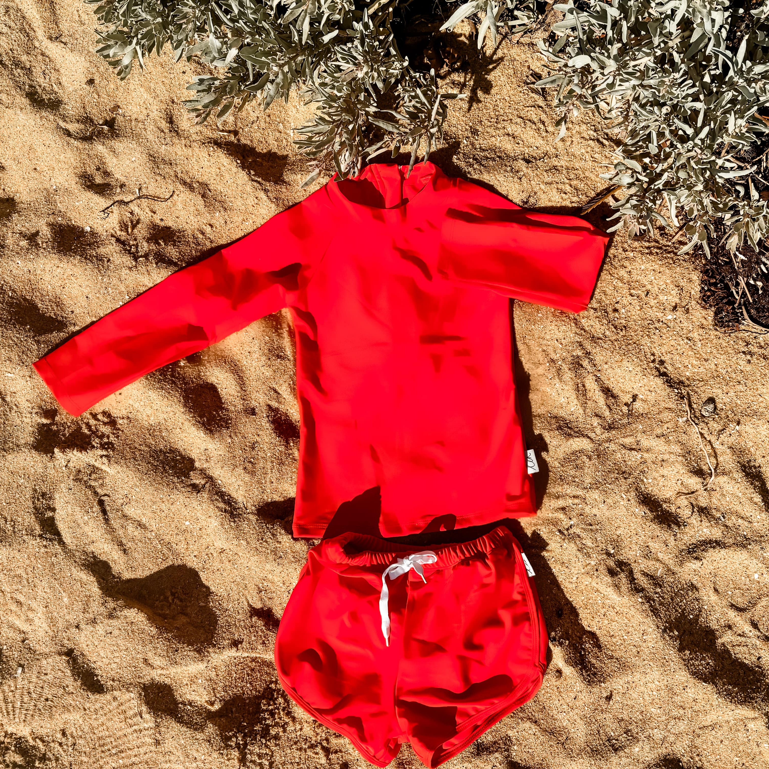 Bright Red children's swimsuit set on sandy ground with plants
