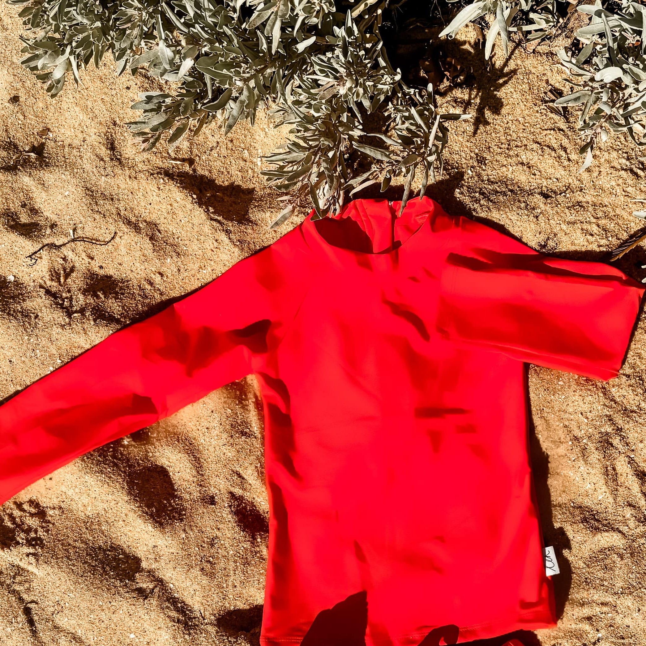 Bright Red children's swimsuit set on sandy ground with plants