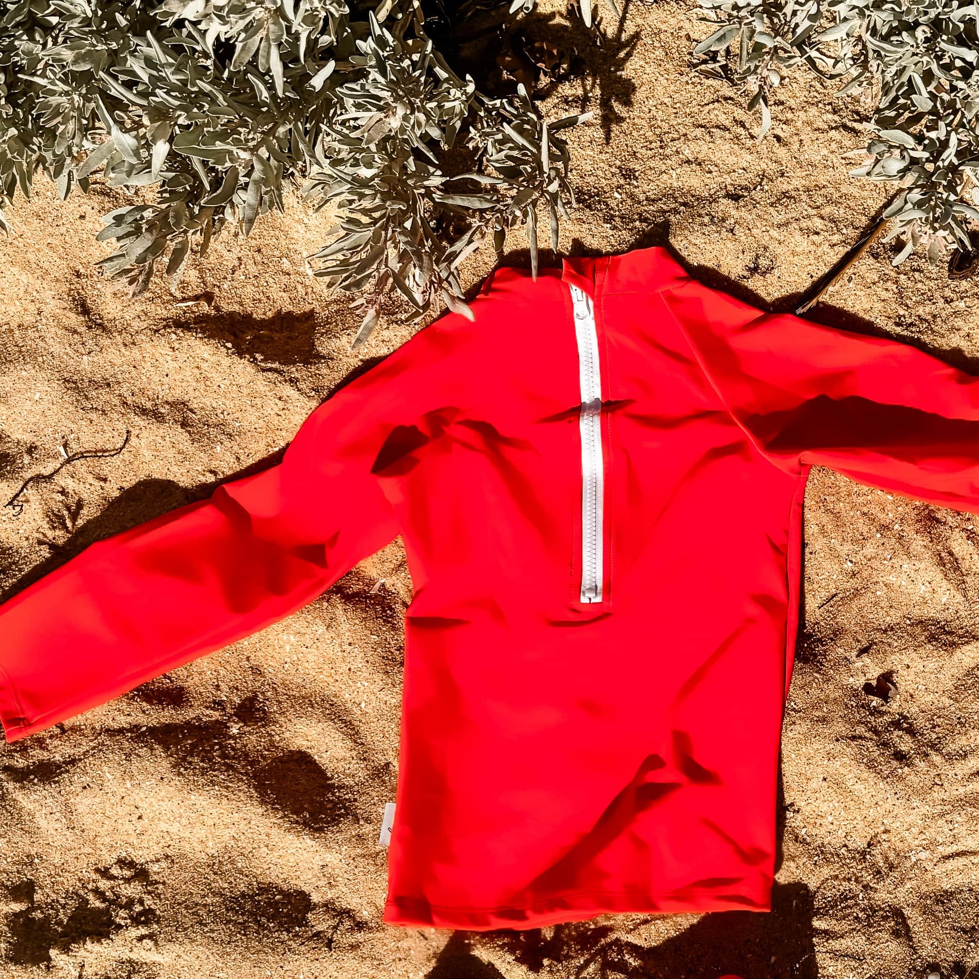 bright boys rash set Red outfit laid out on sandy ground with plants in the background