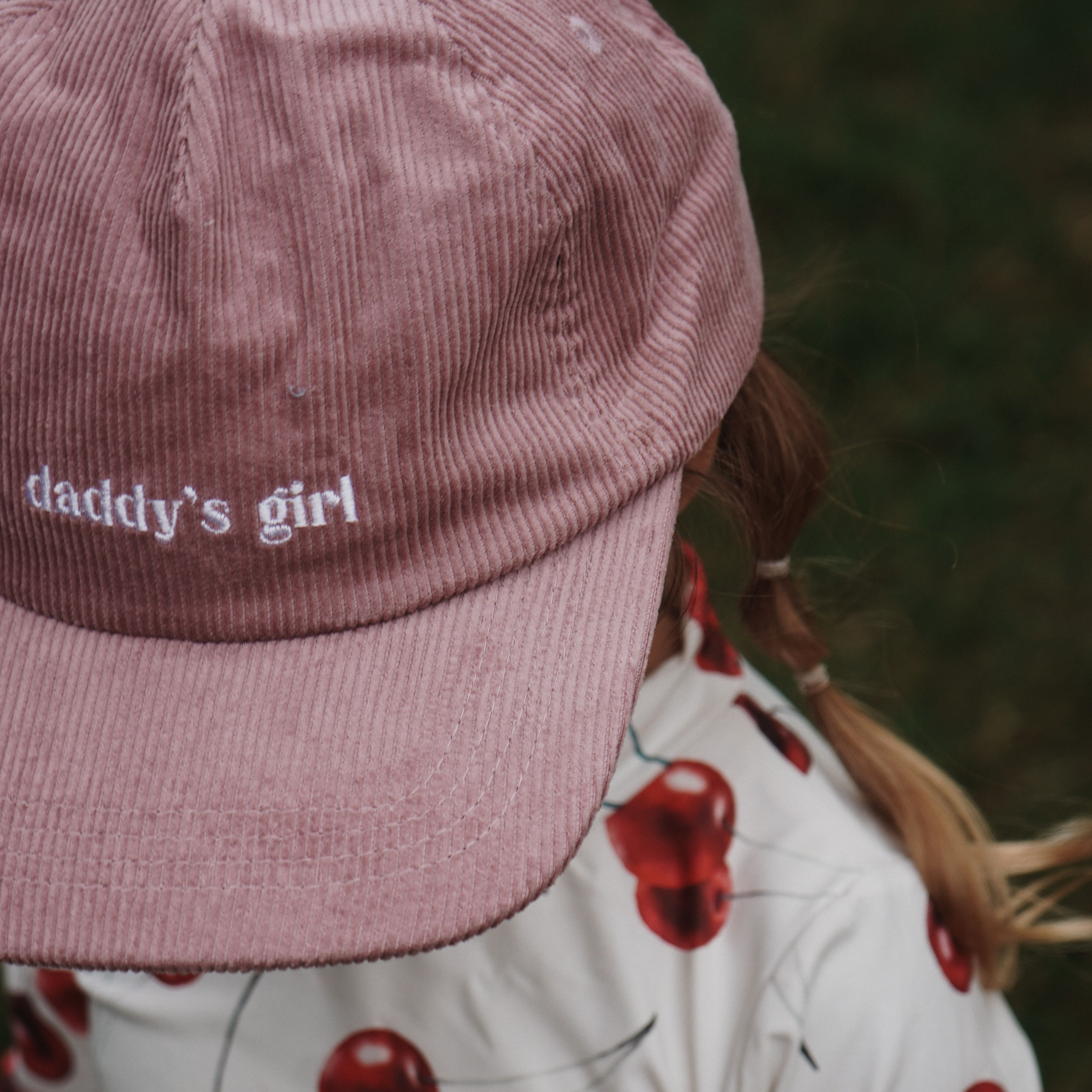 Person wearing a pink 'daddy's girl' fathers day gift cap and cherry-patterned outfit.