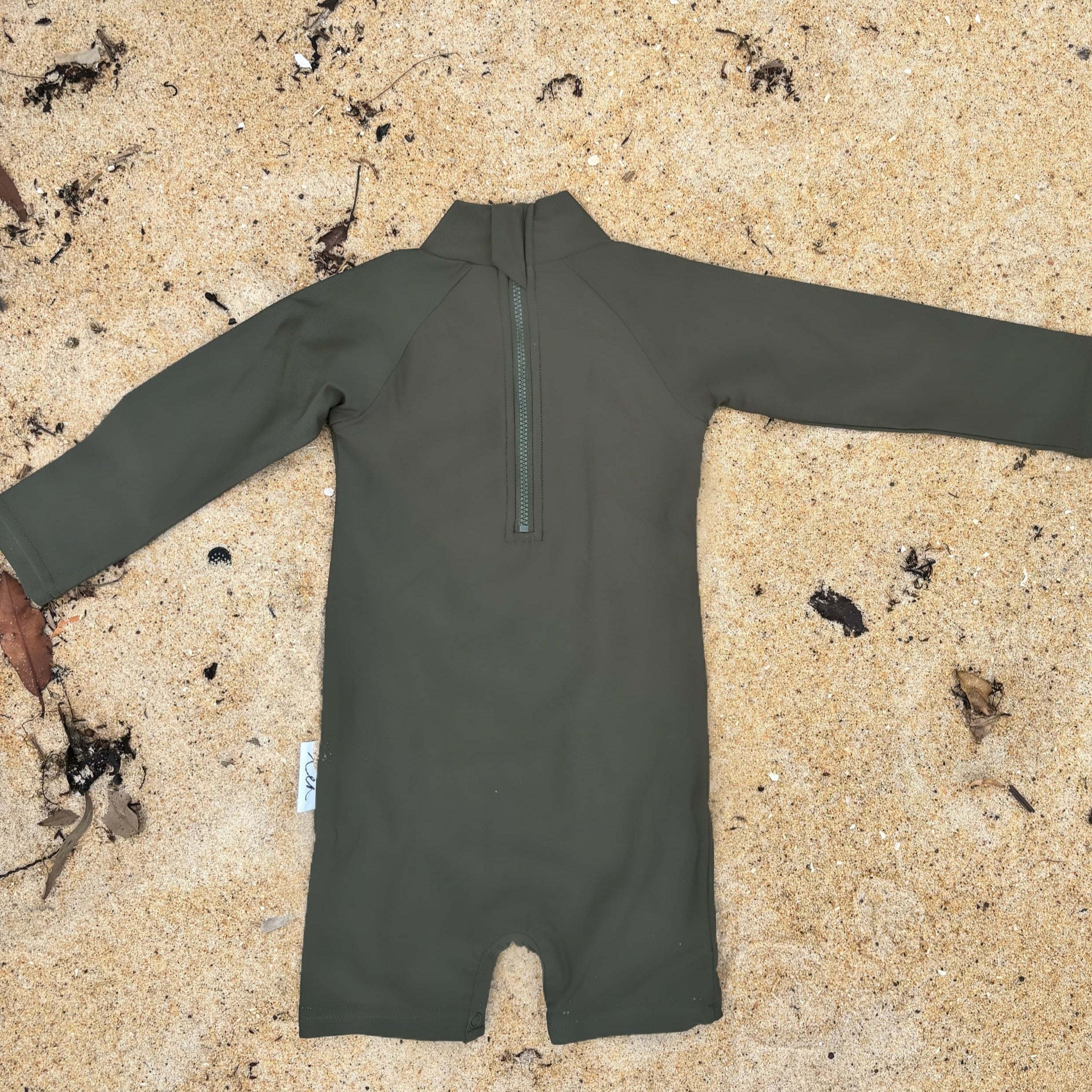 Dark Green swimsuit on a sandy surface with plants in the background