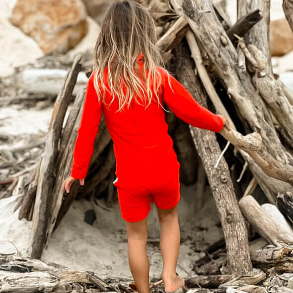 young child playing at beach in a bright neon red one piece rashie