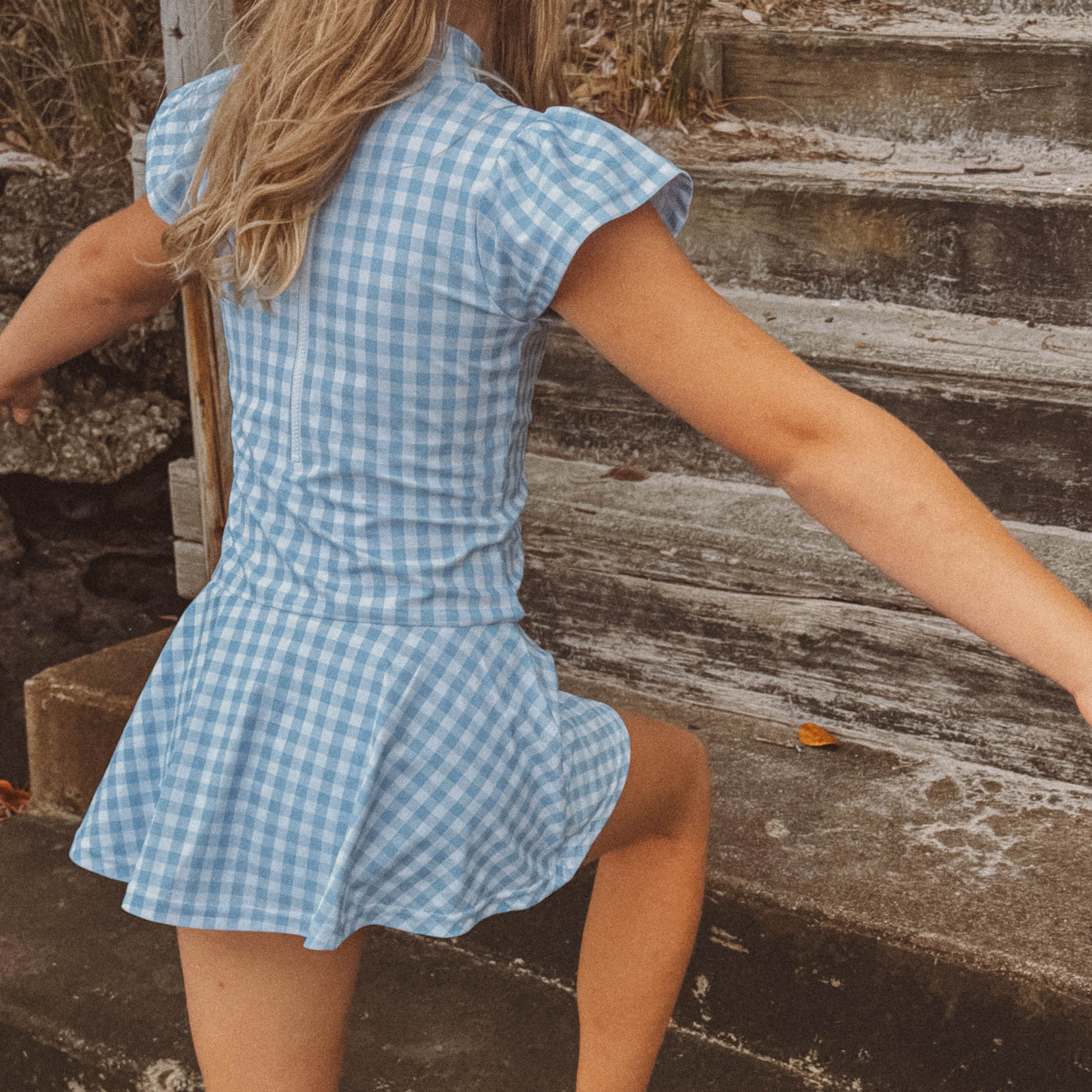 young girl in a blue checkered swim dress standing on stone steps.