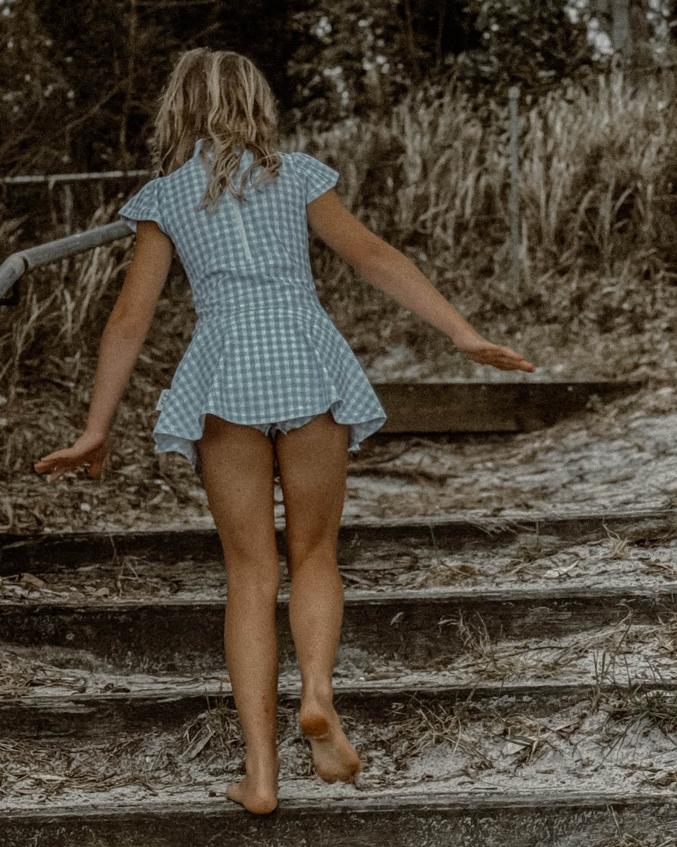 girls swimsuit in a checkered dress walking on wooden steps outdoors