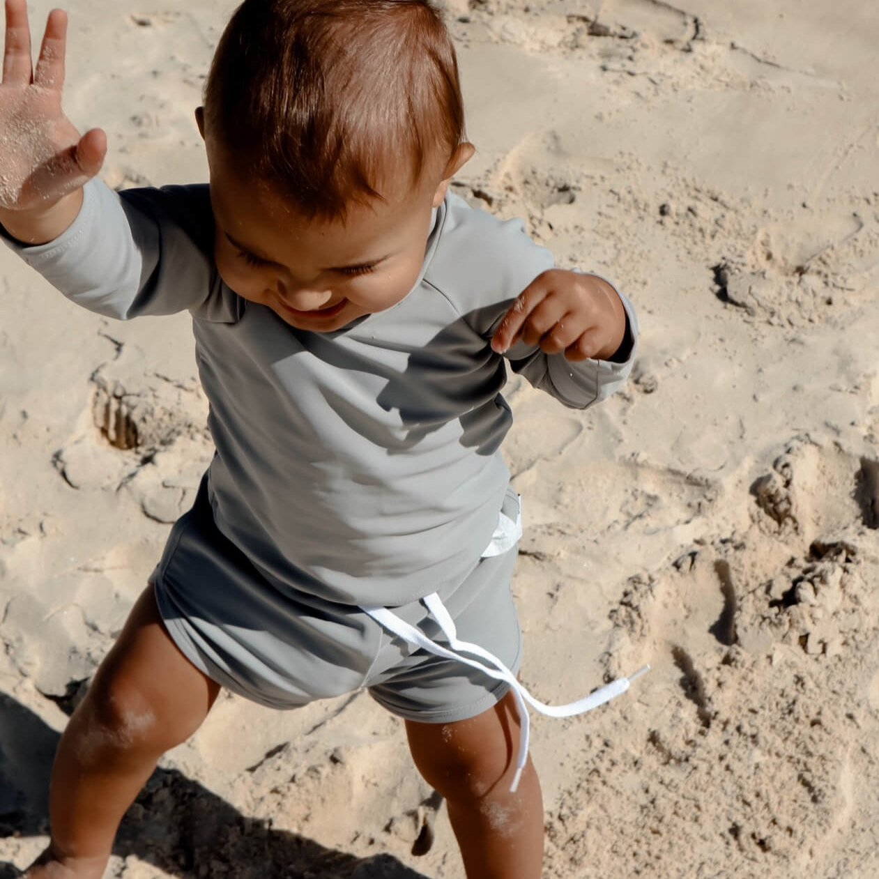 baby boy playing in a grey two piece sun safe rash set