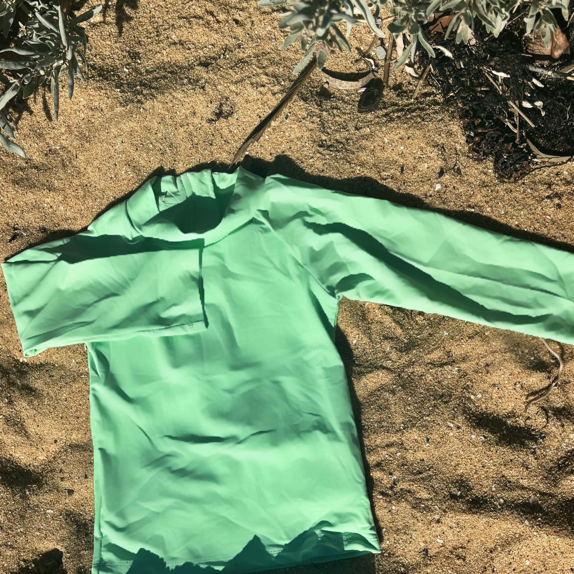 bright high vis Green children's swimsuit set on sandy ground with plants in the background