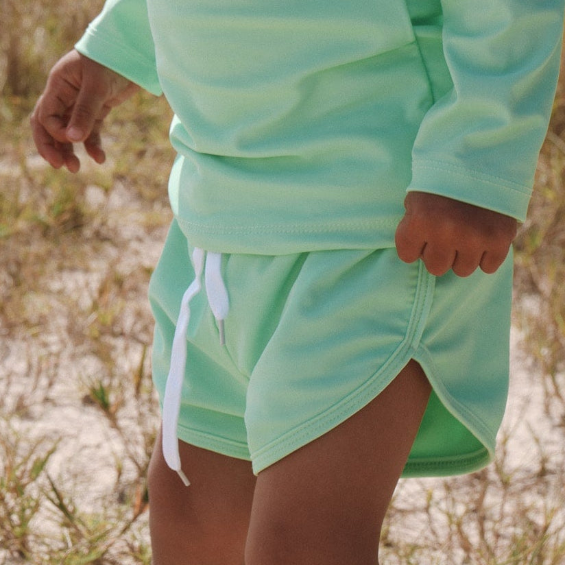 Child wearing a bright light green swim short outfit and cap outdoors