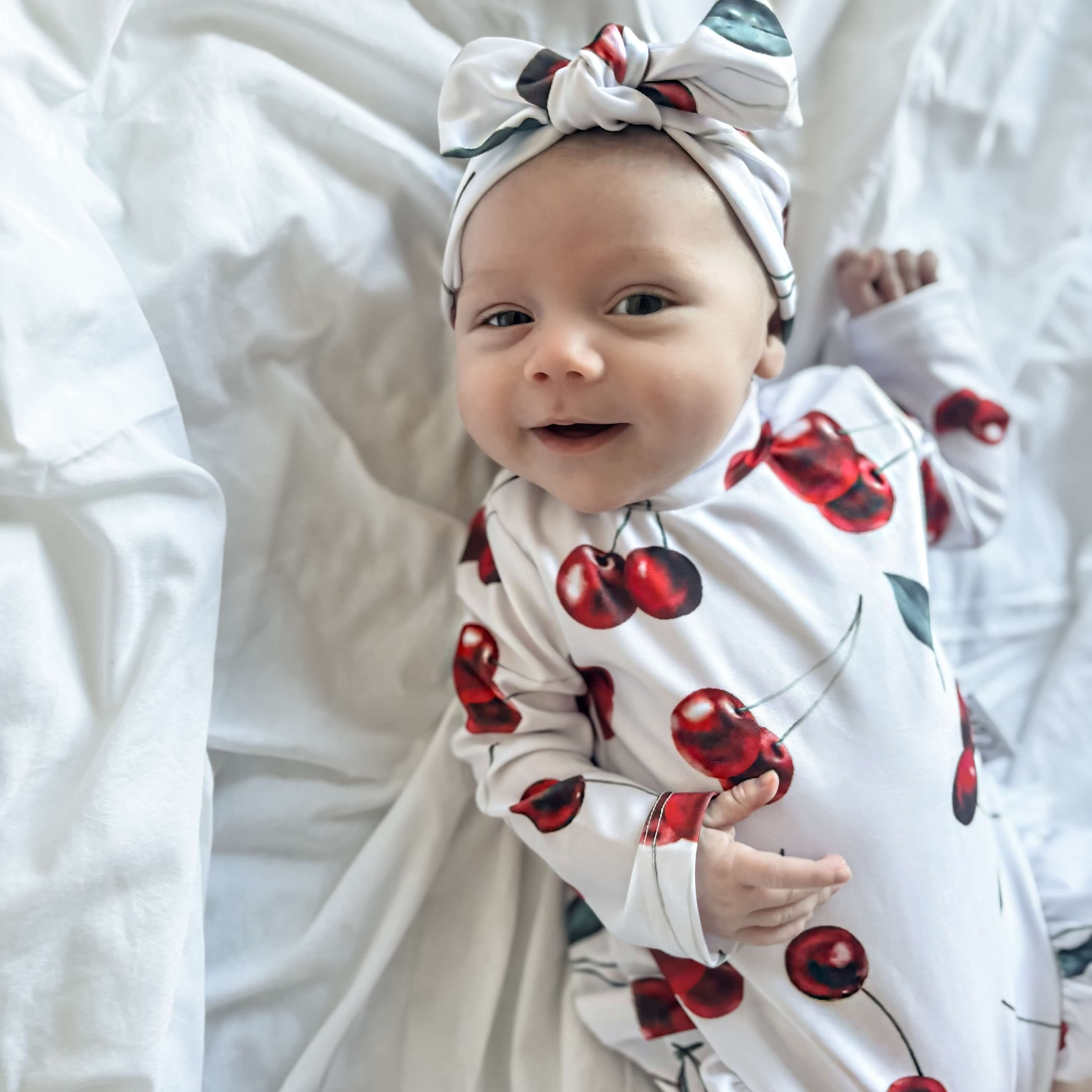 Baby wrapped in a cherry-patterned swimsuit a headband on a white background