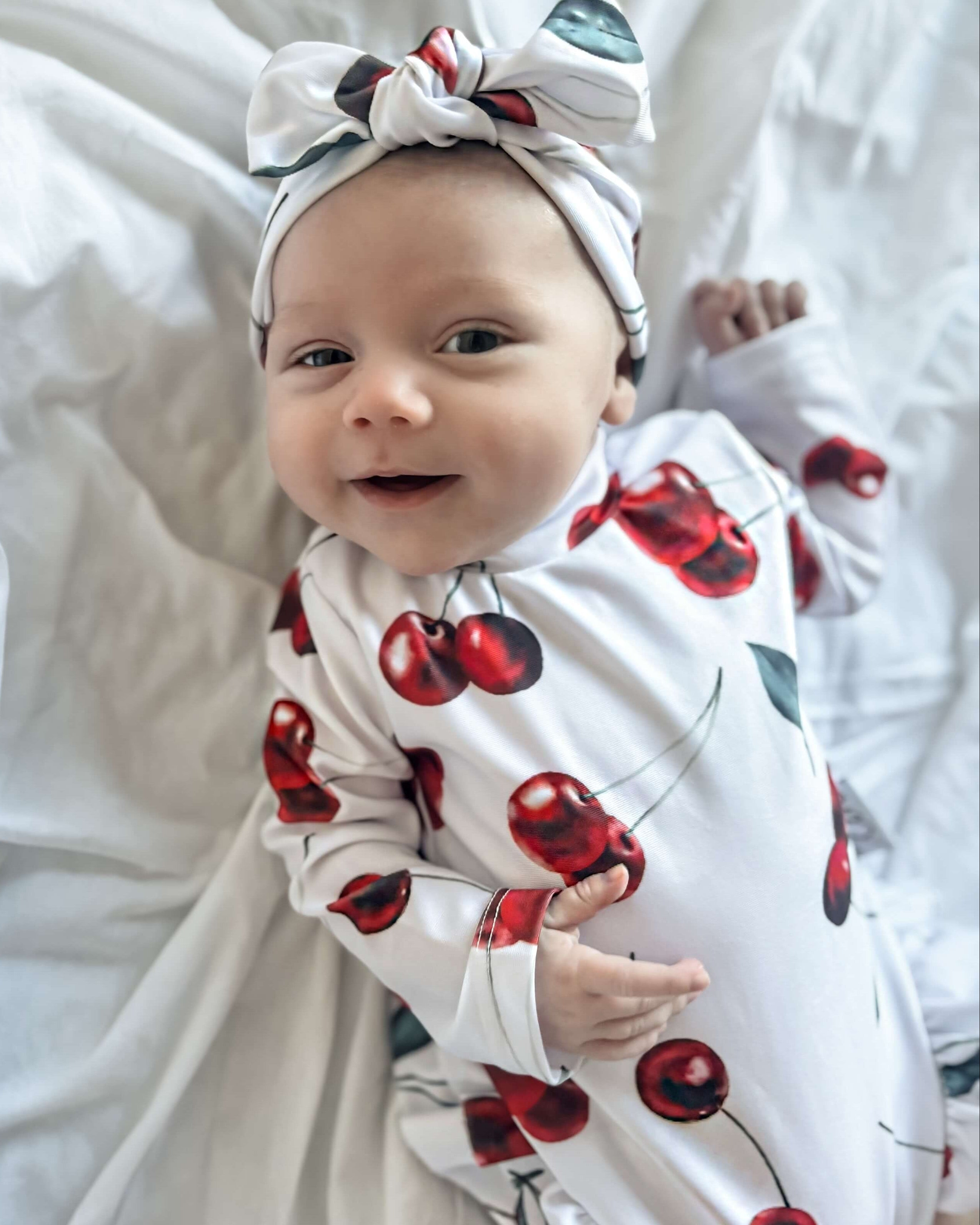 Baby wrapped in a cherry-patterned swimsuit a headband on a white background