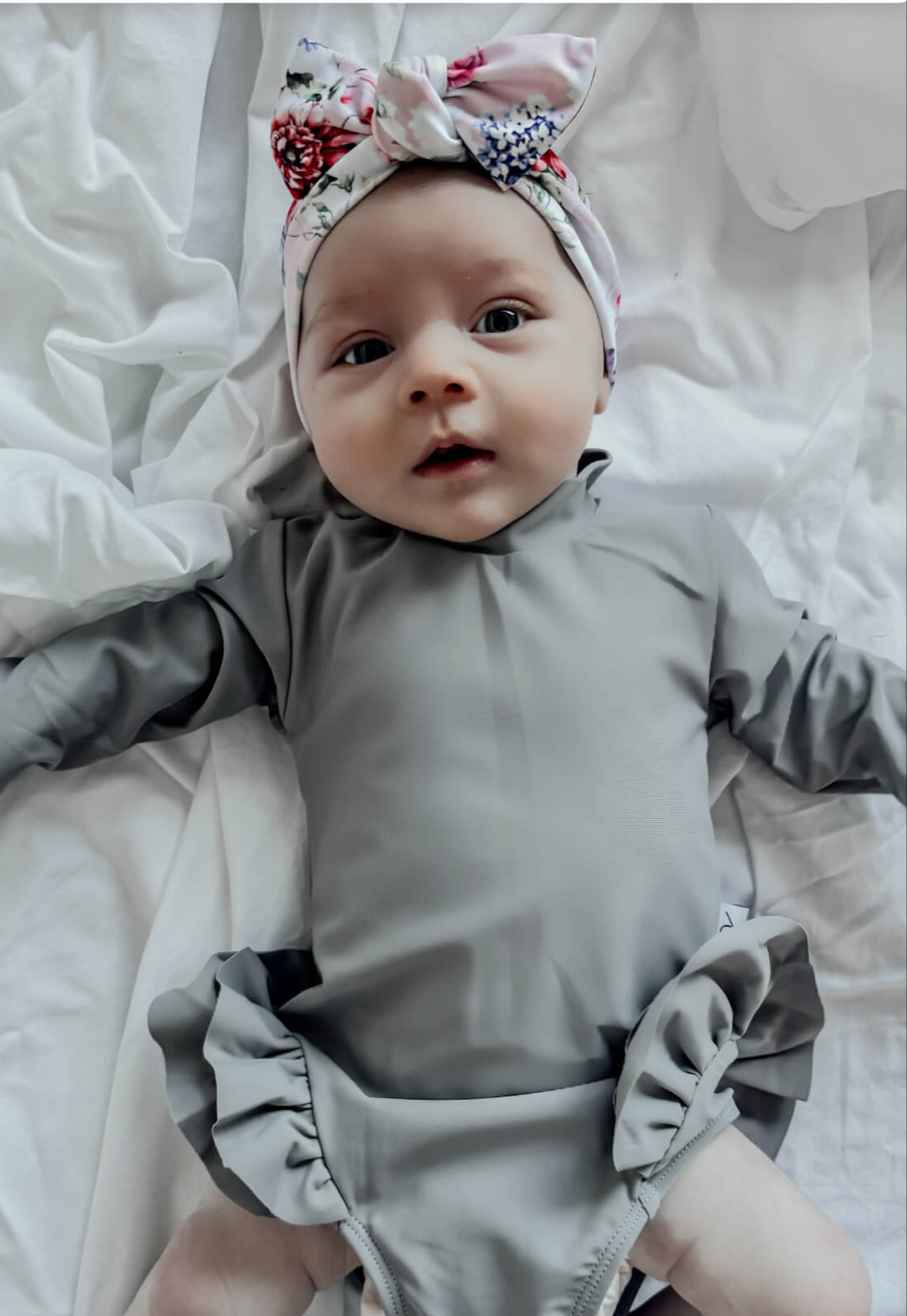 newborn swimsuit for baby girl with nappy change snaps with a floral headband lying on a white blanket