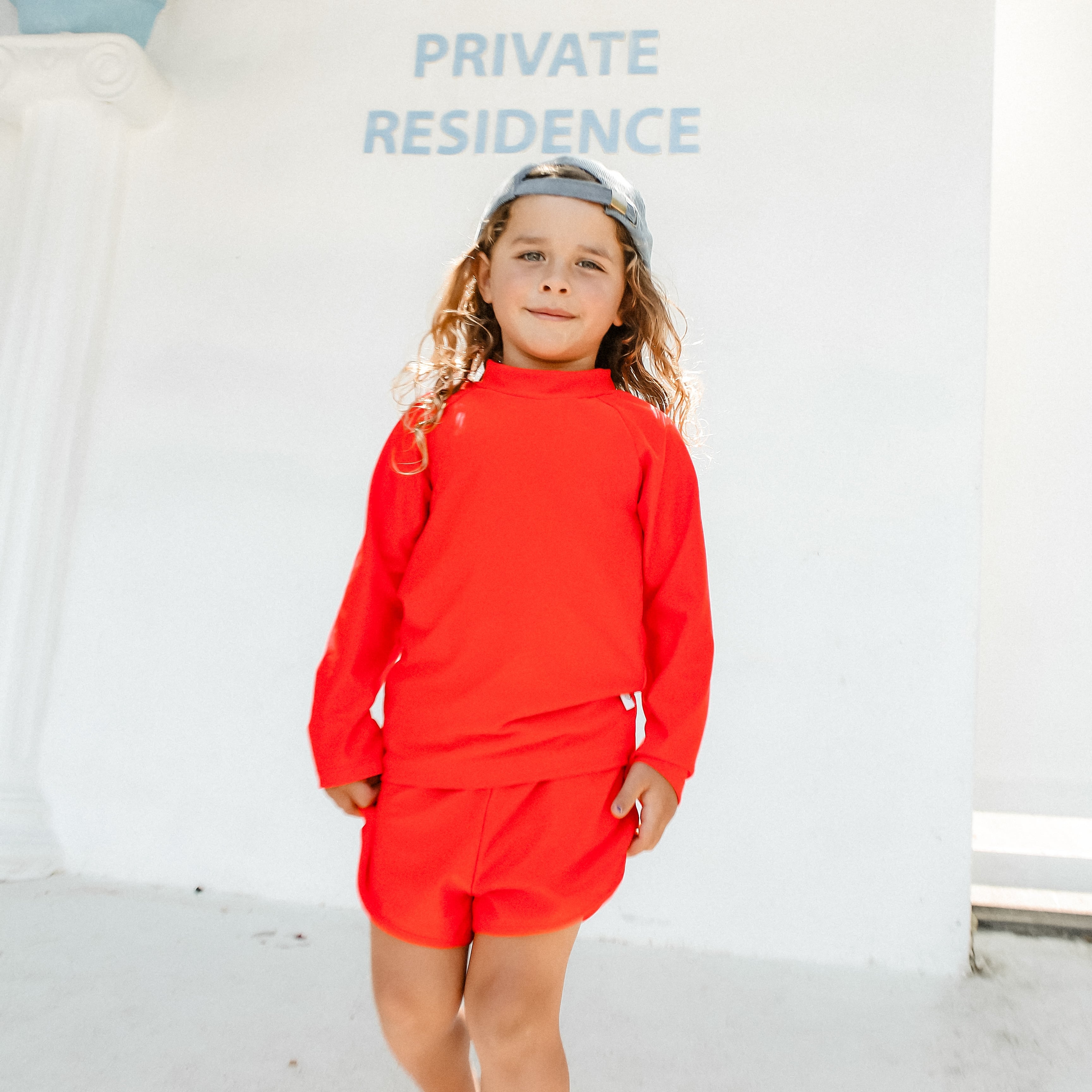 Child wearing a bright red swimsuit standing in front of a 'Private Residence' sign.