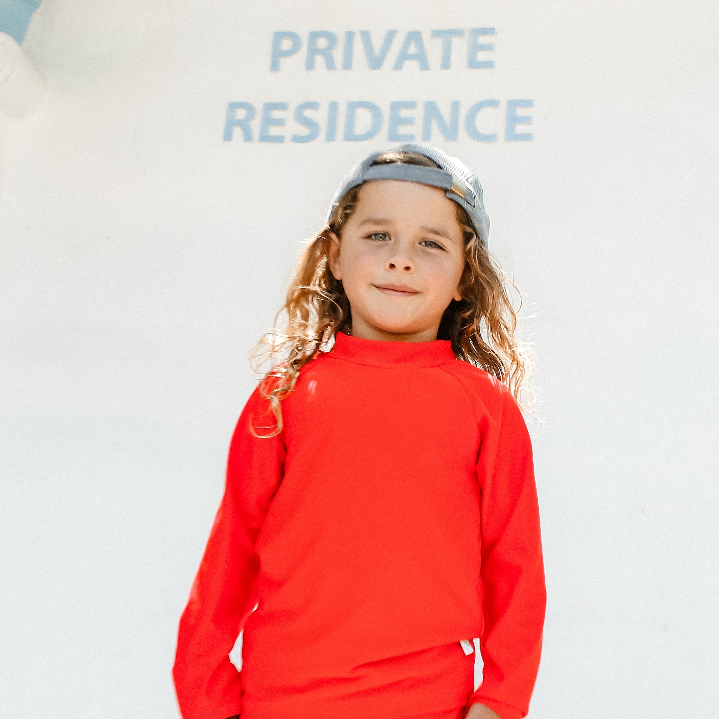 Child wearing a bright red swimsuit standing in front of a 'Private Residence' sign.