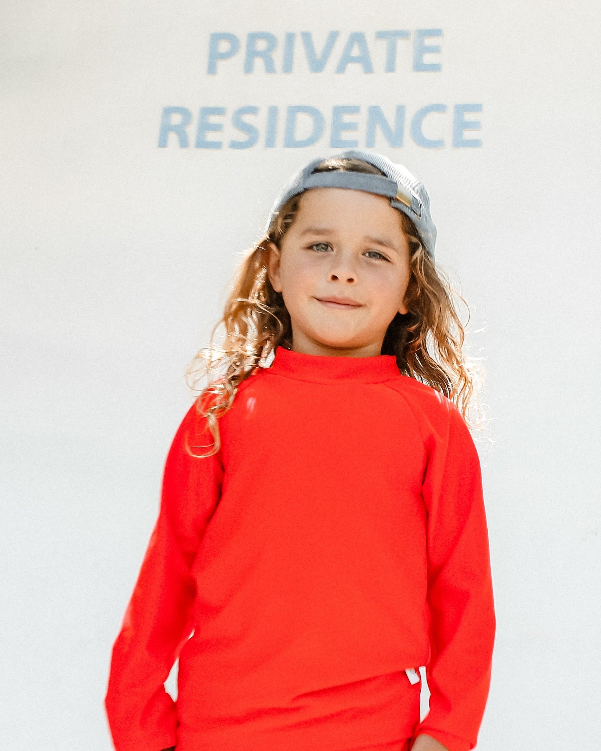 Child wearing a bright red swimsuit standing in front of a 'Private Residence' sign.