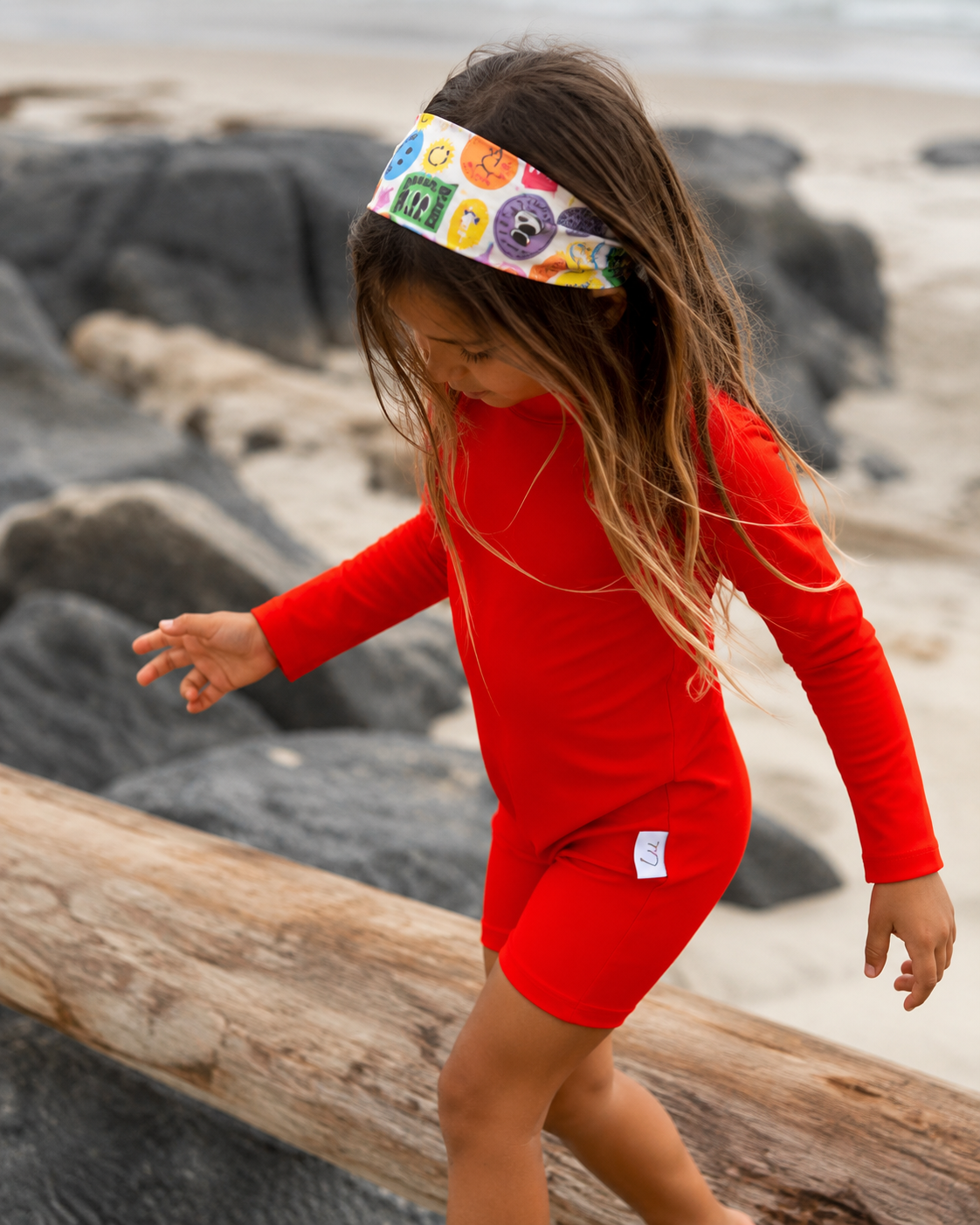 Child in a bright
red swimsuit on a beach with a colorful headband