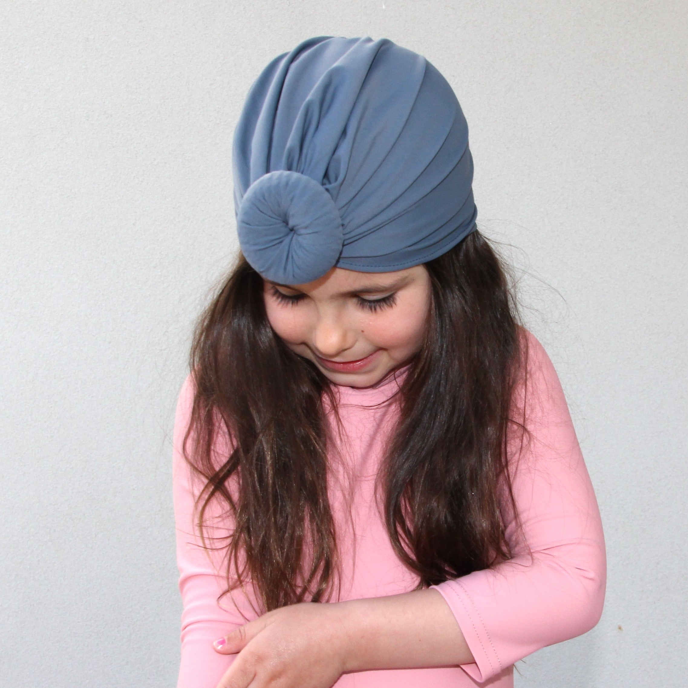 Little girl wearing pink long sleeve swimsuit and navy swim turban
