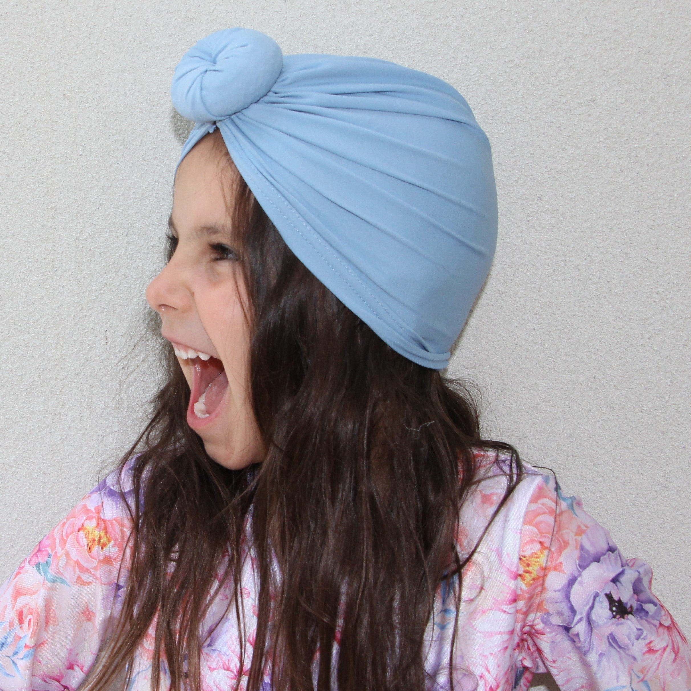 Young girl laughing wearing a floral bathing suit, and blue swim turban