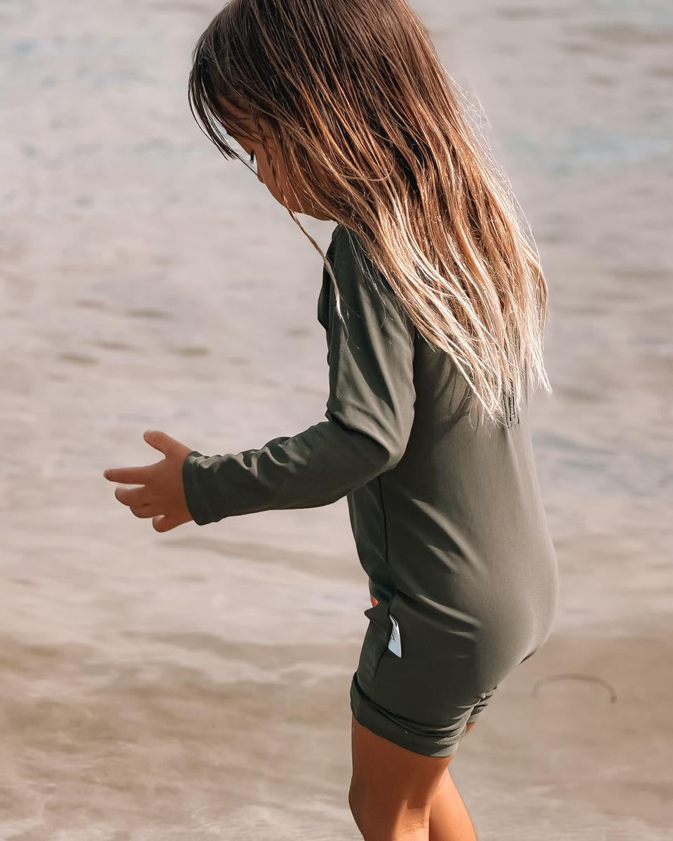 Child playing in shallow water wearing a green swimsuit.