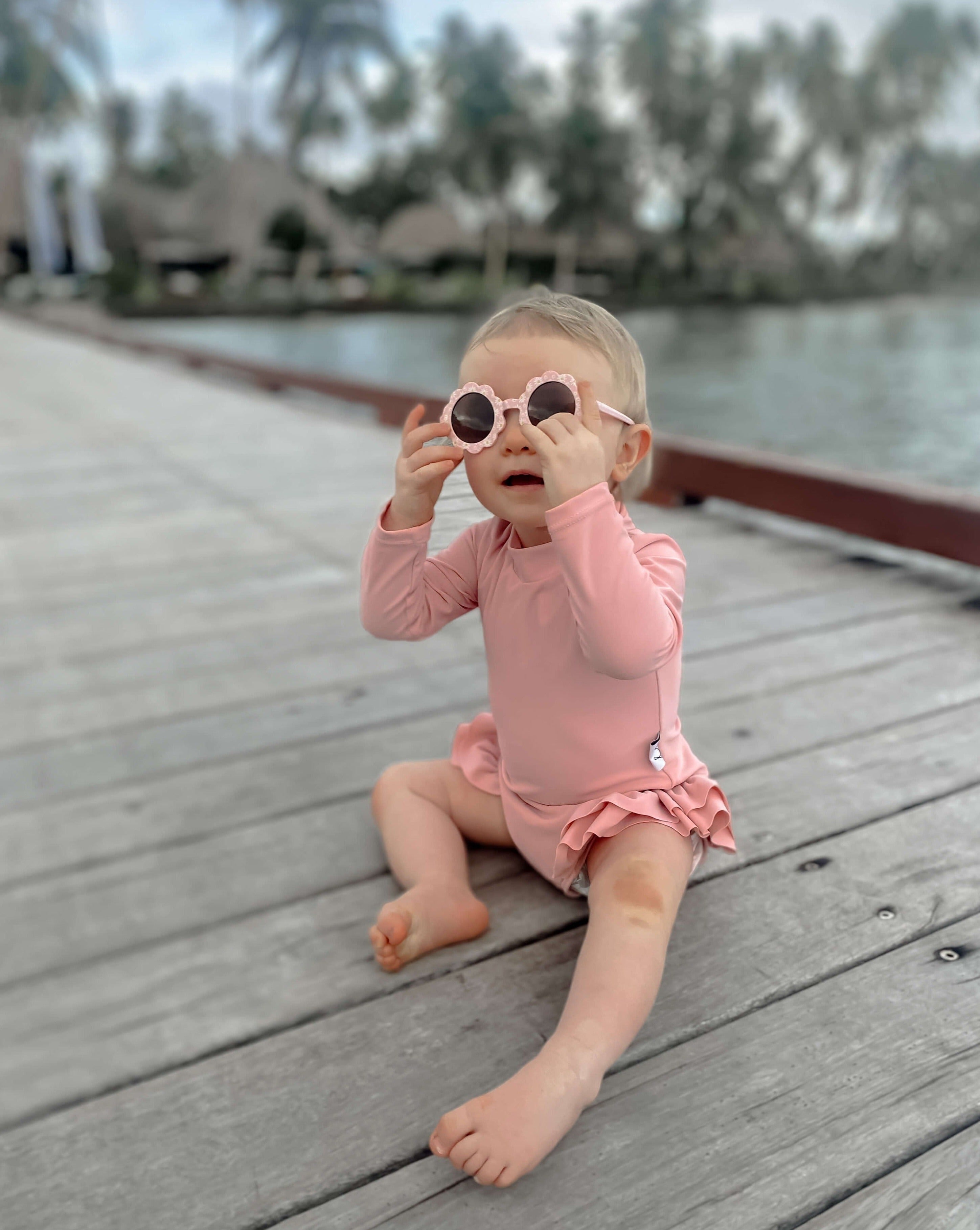 Baby girl wearing sunglasses and a pink long sleeve swimsuit