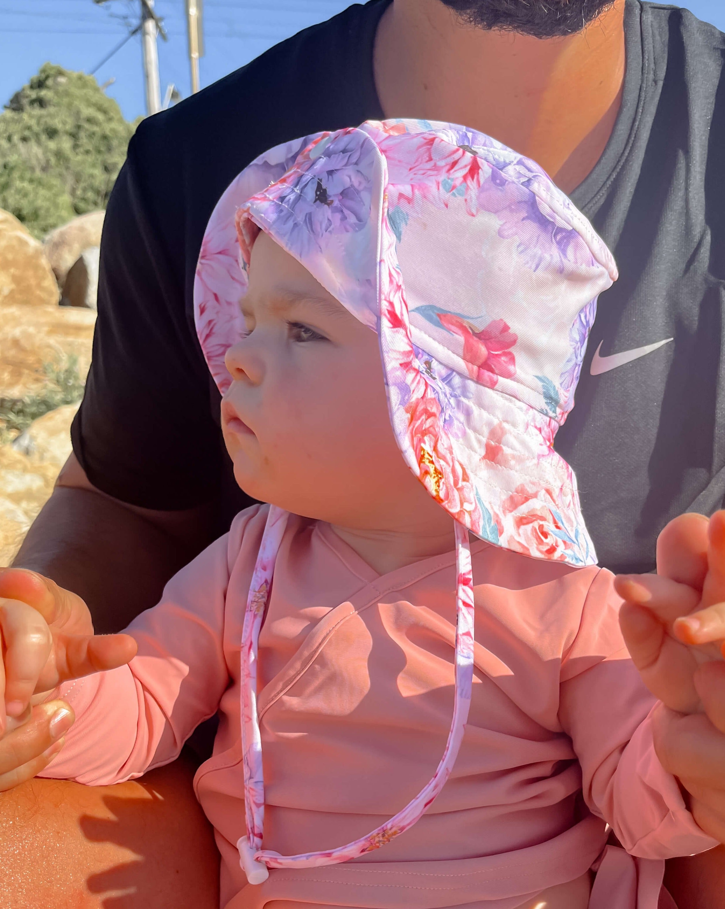 Baby girl on the beach with her dad wearing a sun hat