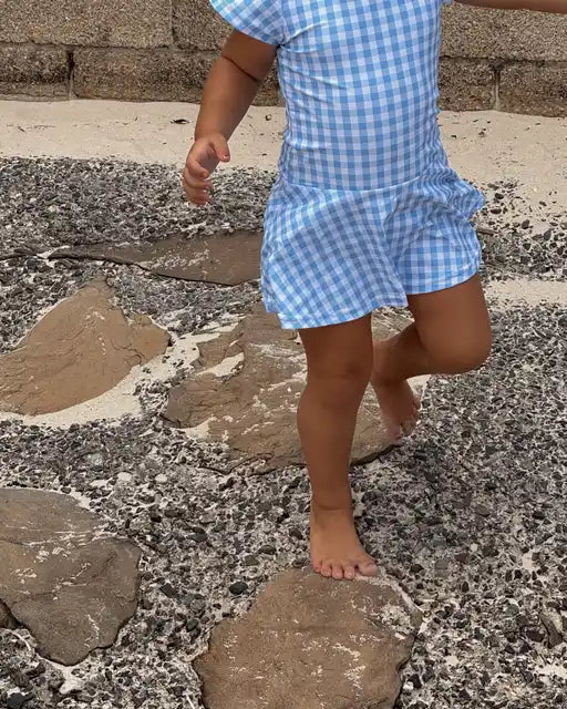 Child wearing a blue checkered swimsuit dress  outfit walking on stone steps.