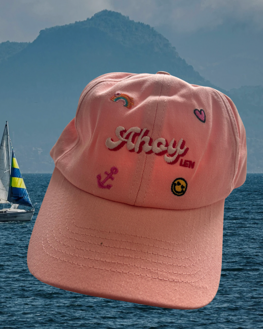 Pink cap with embroidered designs on a scenic background of water and mountains