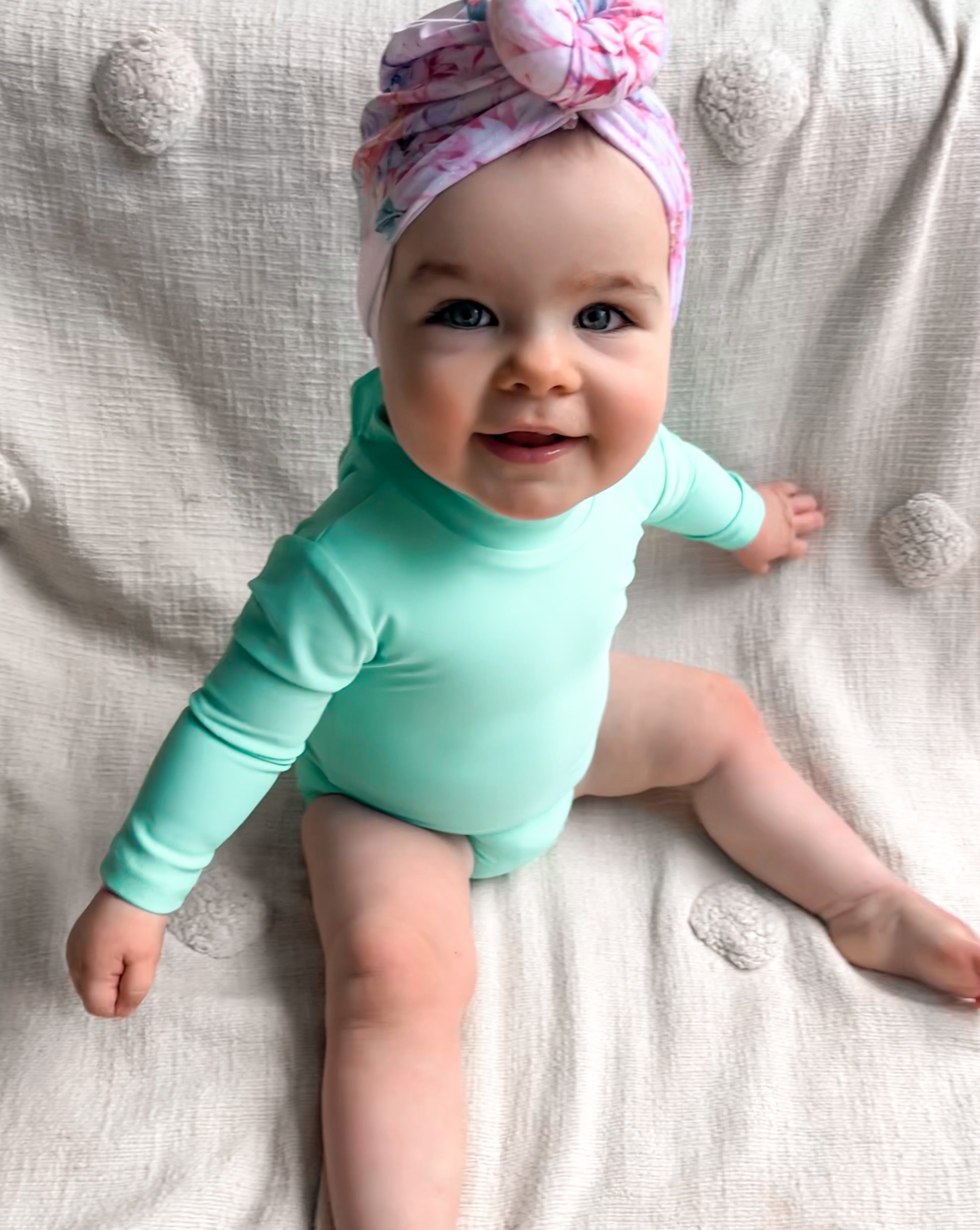 baby girl in  a bright green long sleeve nappy change swimsuit and swim turban