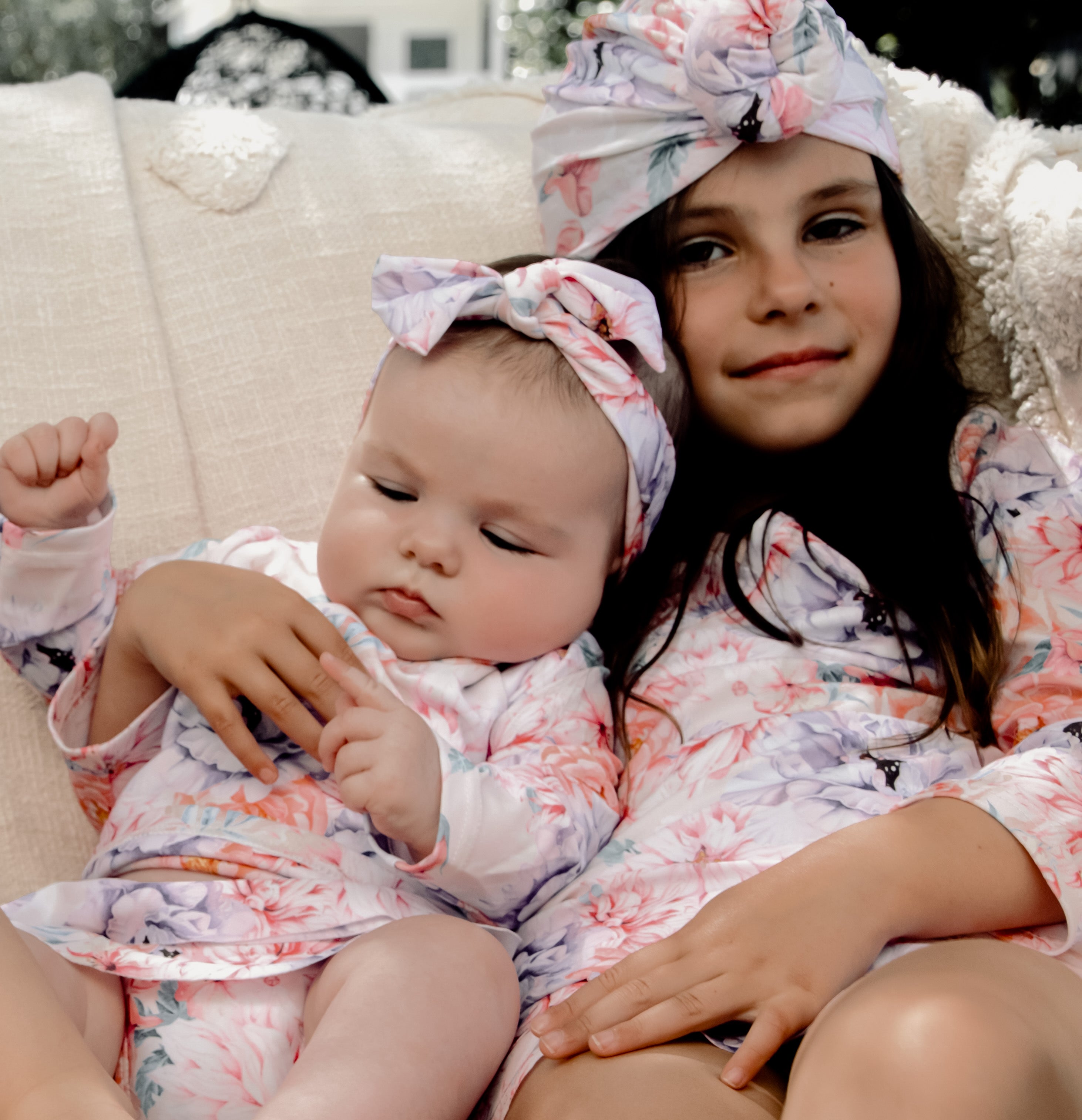 A baby and young girl in long sleeve floral swimwear that is matching