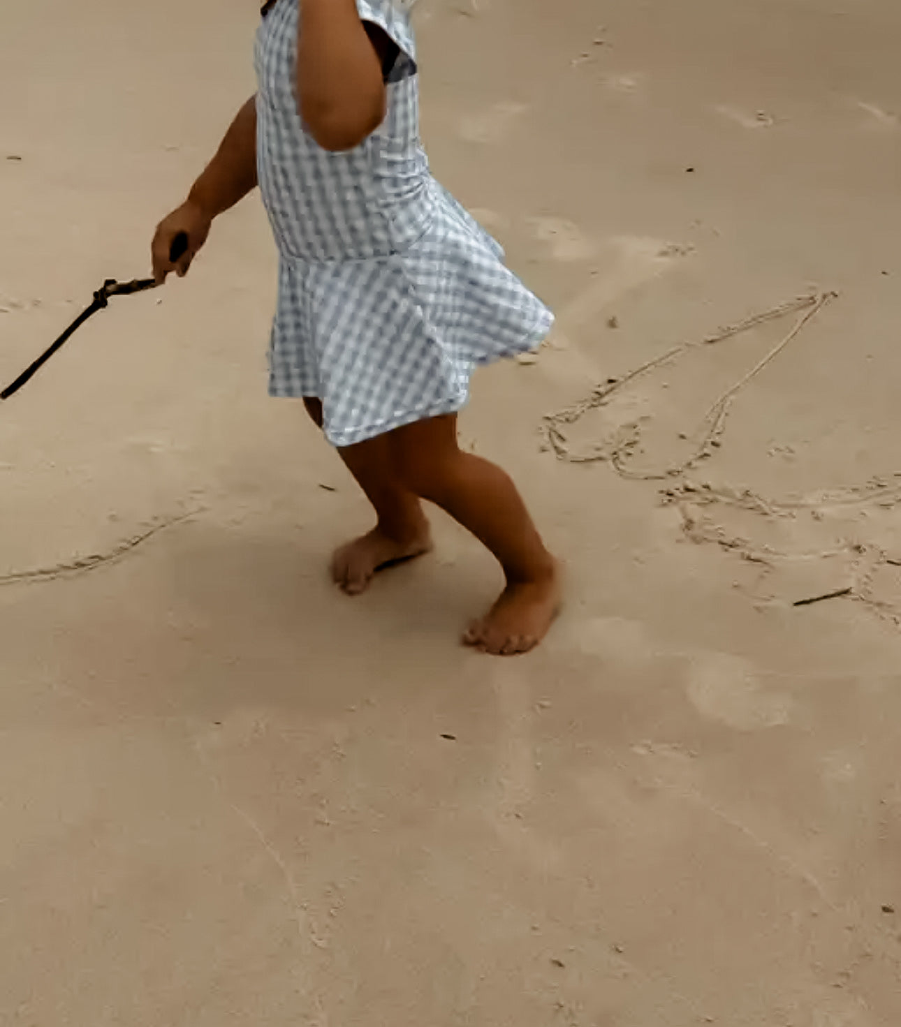 Person in a checkered dress walking on sand with a leash.