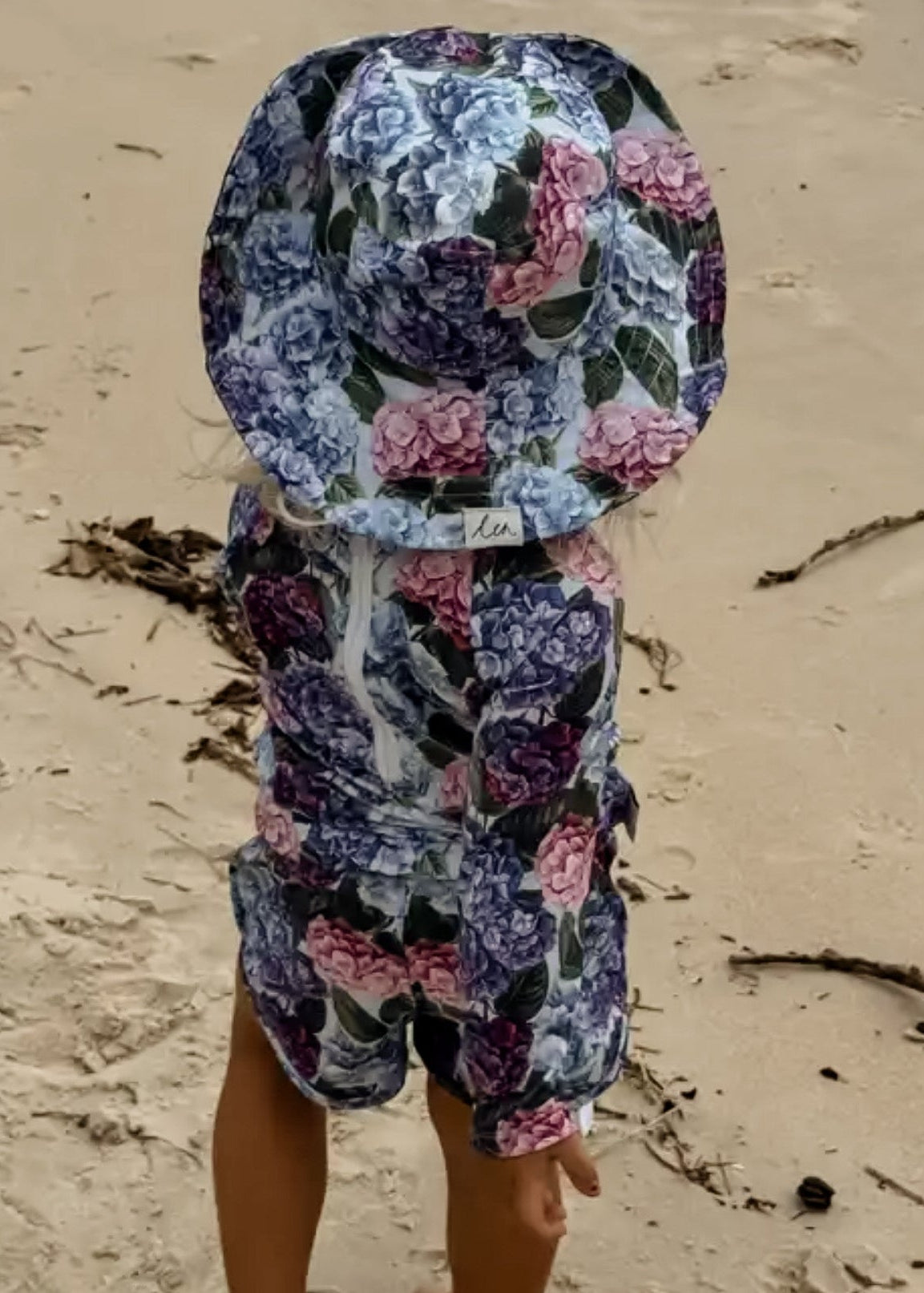 Child wearing a floral swim sun hat and rash swim set on a sandy beach.