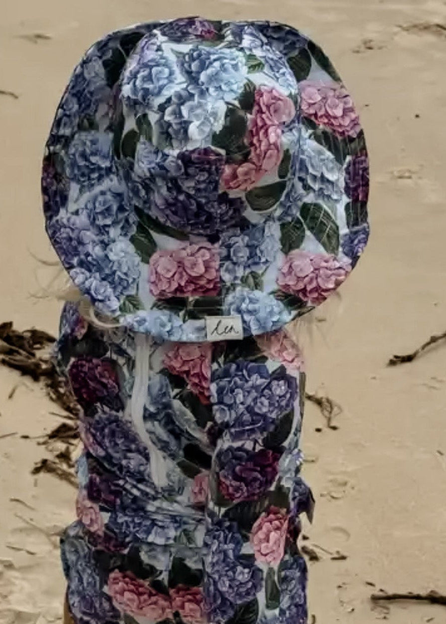 Child wearing a floral swim sun hat and rash swim set on a sandy beach.