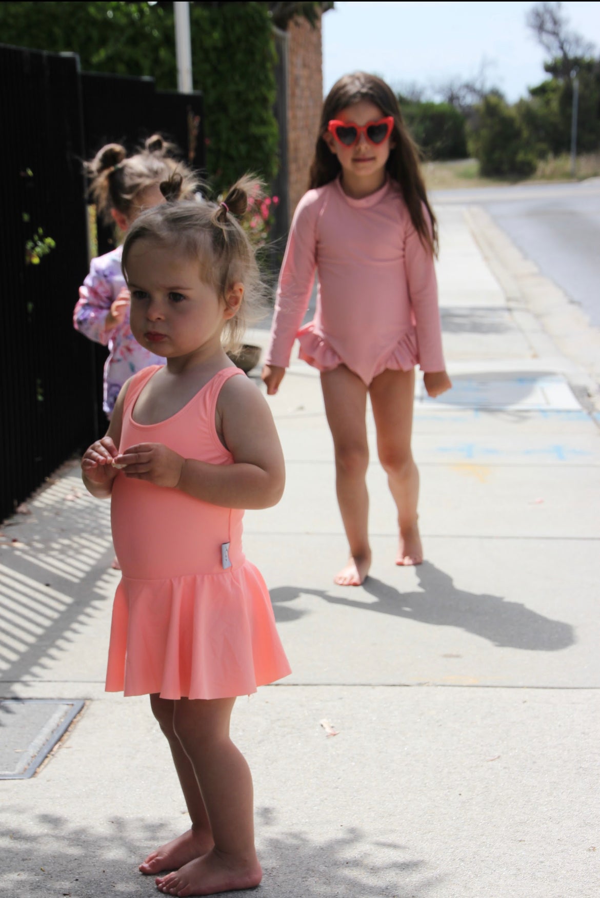 toddlers and young girl walking to the beach in bright, premium swimsuits