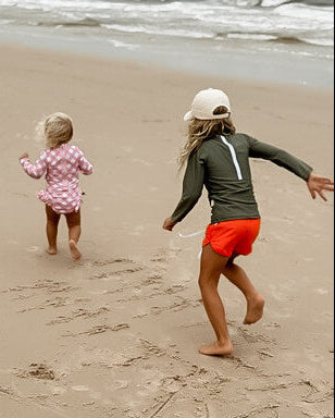 Two children running on a sandy beach with ocean waves in the background