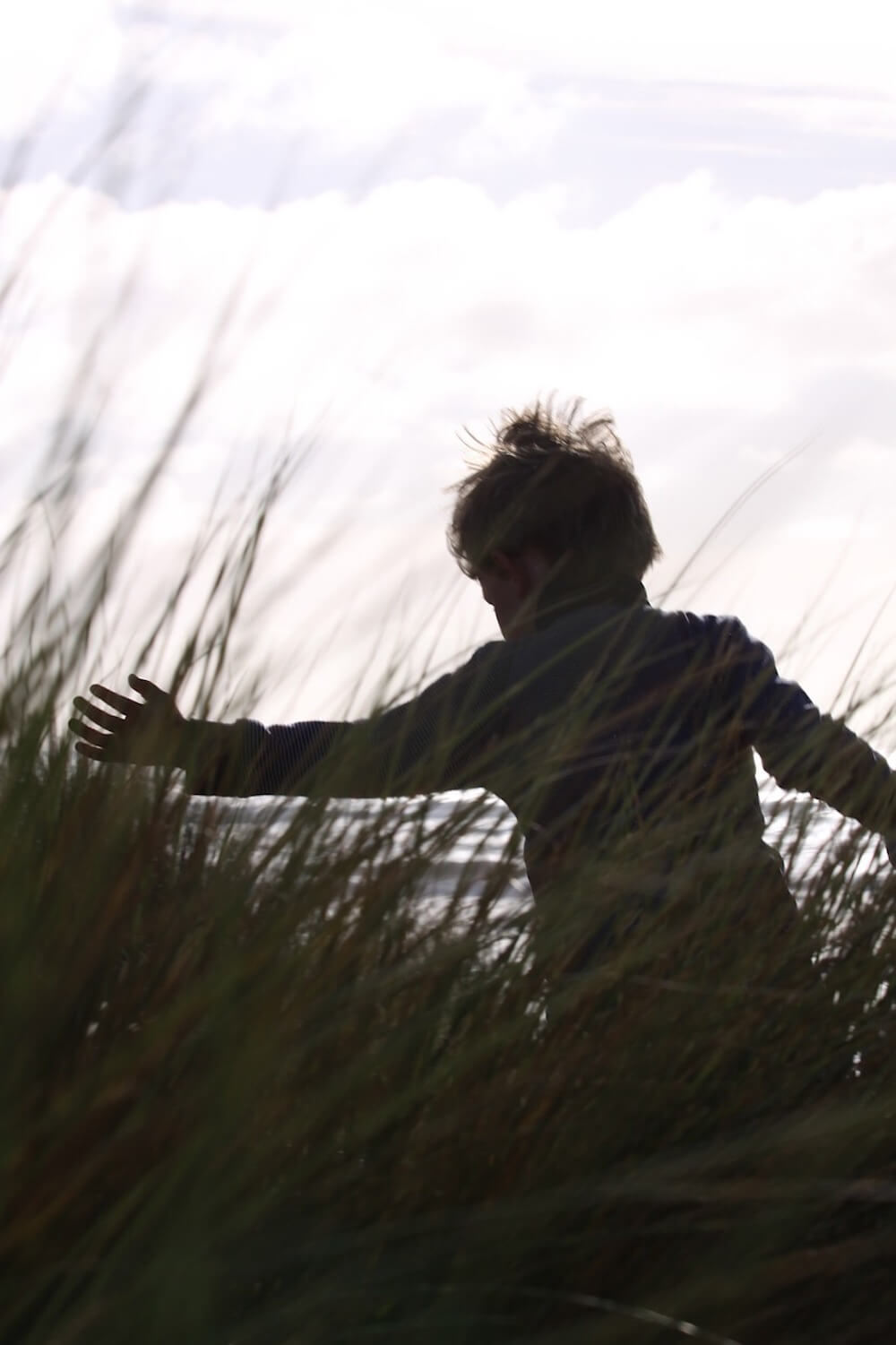 a boy playing in the grass on the beach