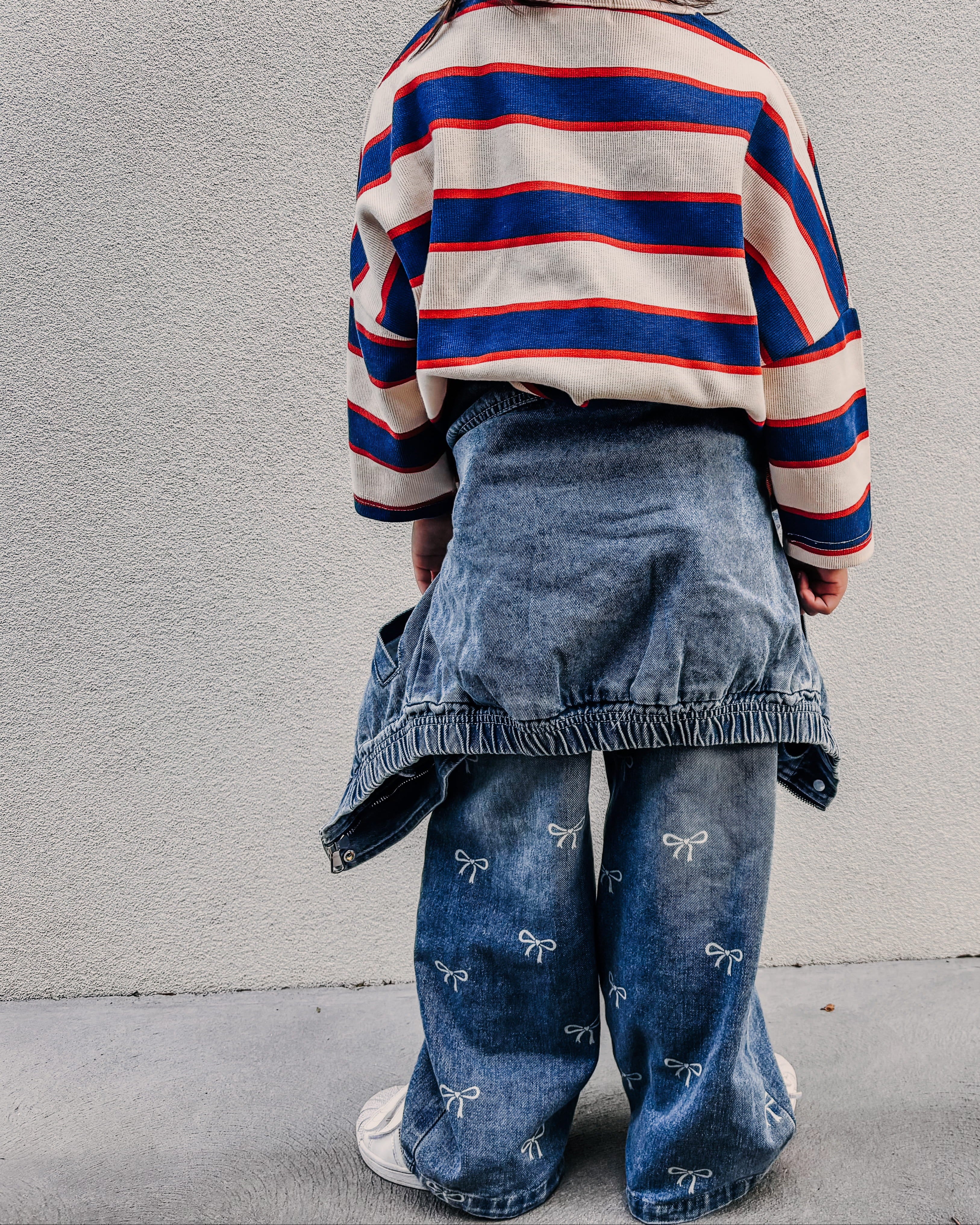 Person wearing a striped sweater and denim skirt against a plain wall.