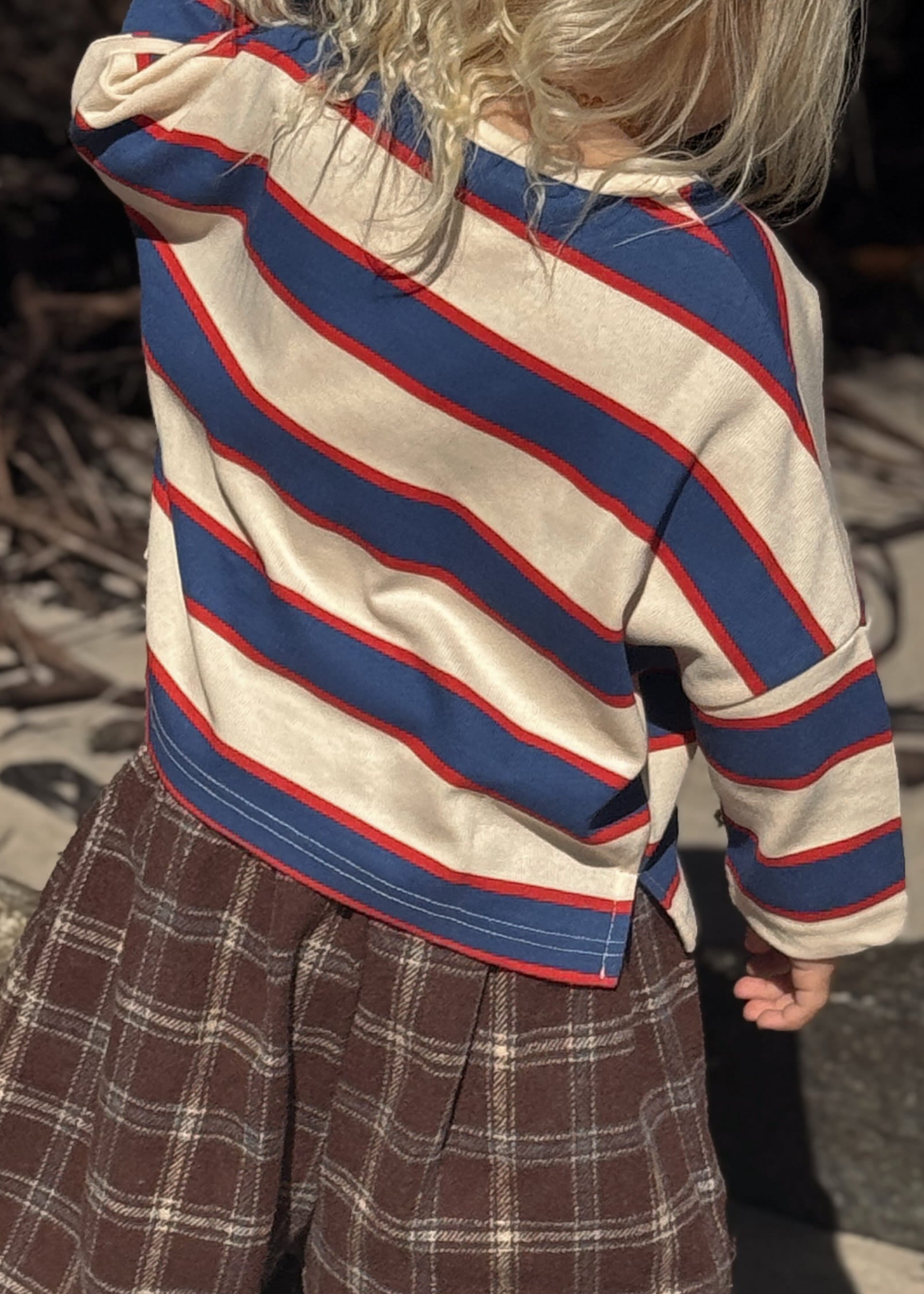 Child wearing a striped sweater and plaid pants standing on a stone surface.