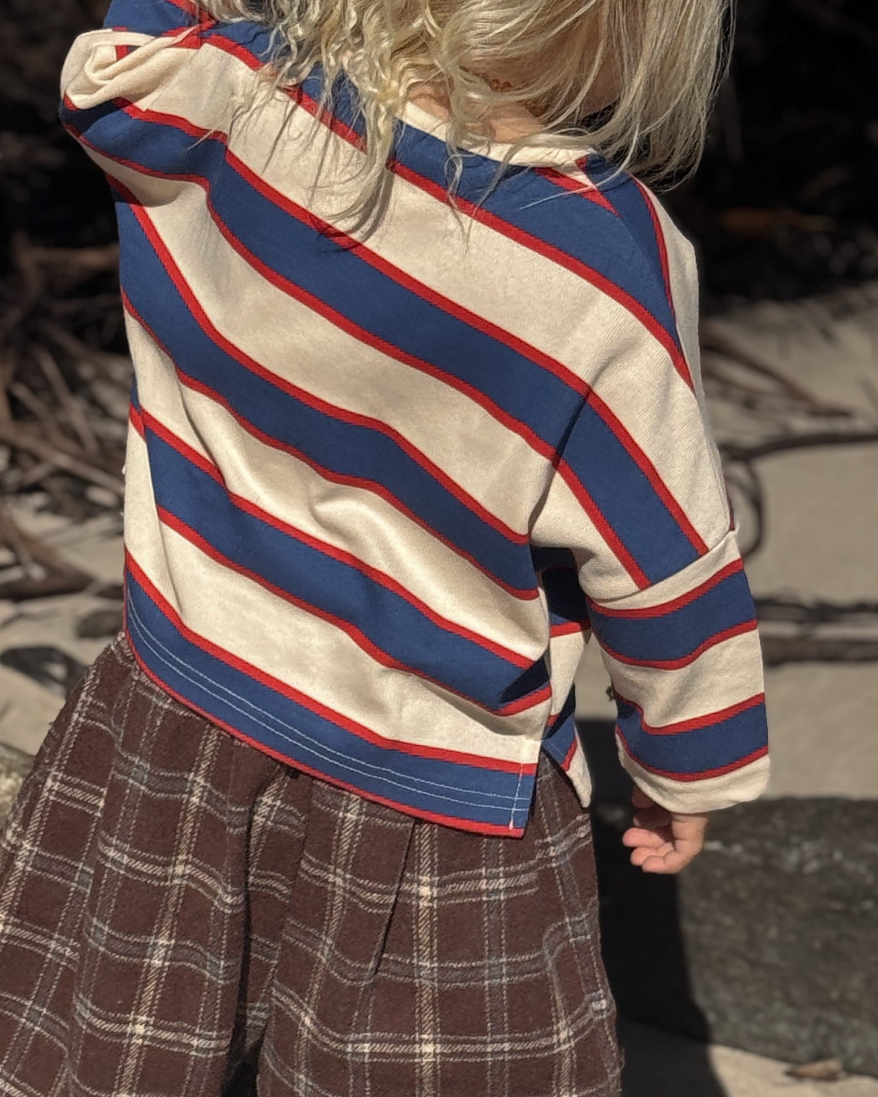 Child wearing a striped sweater and plaid pants standing on a stone surface.