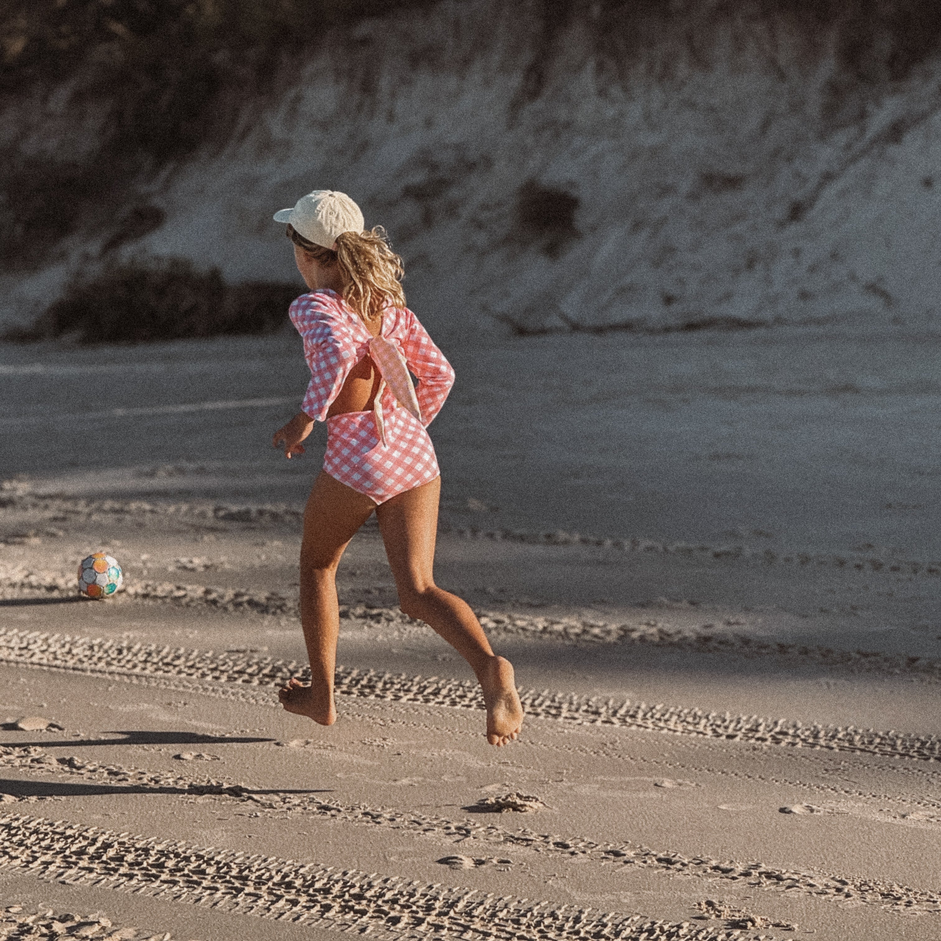 Child running on a sandy beach with a toy in the background