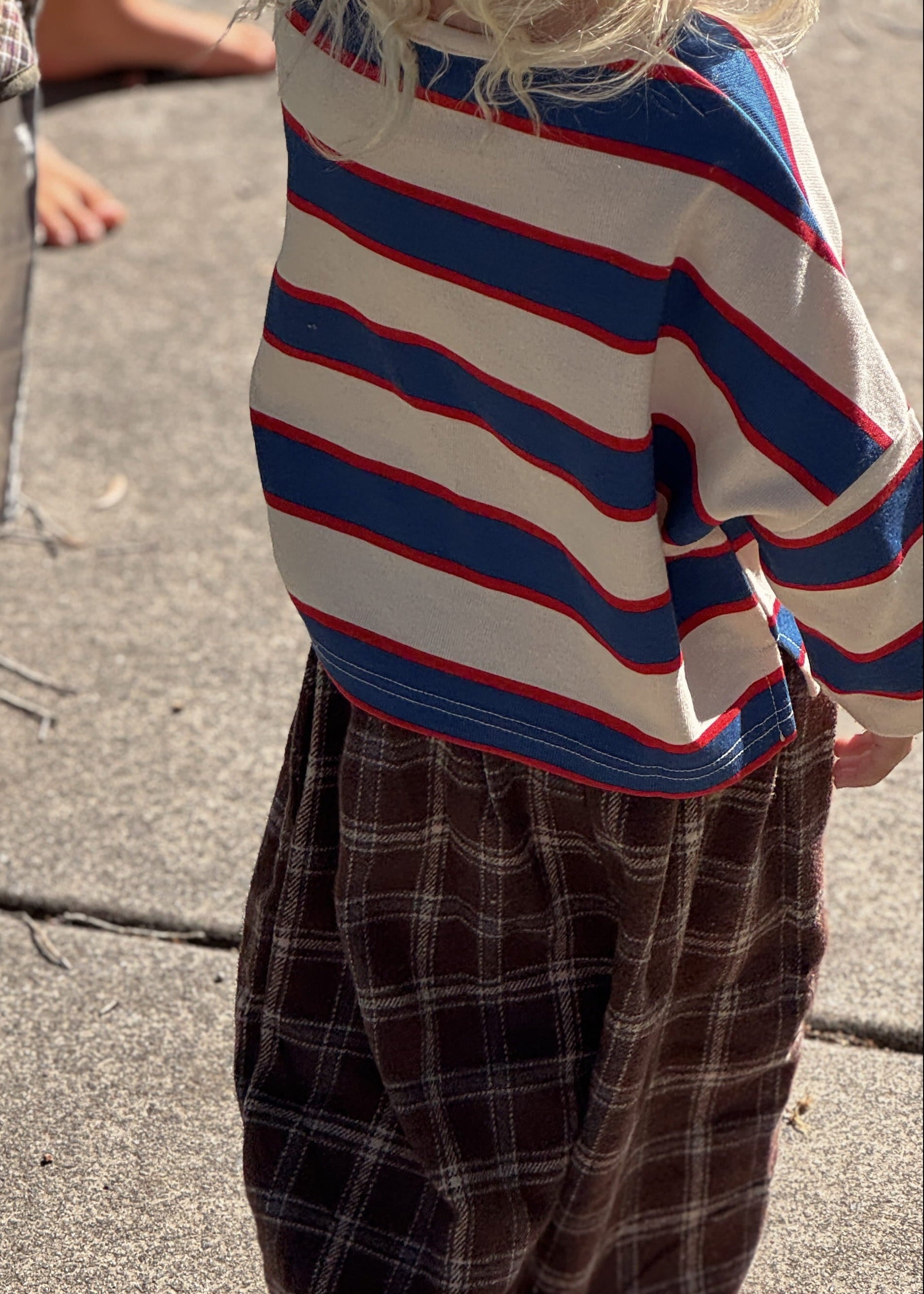 Two children standing on a concrete surface, one wearing a striped sweater and plaid pants.